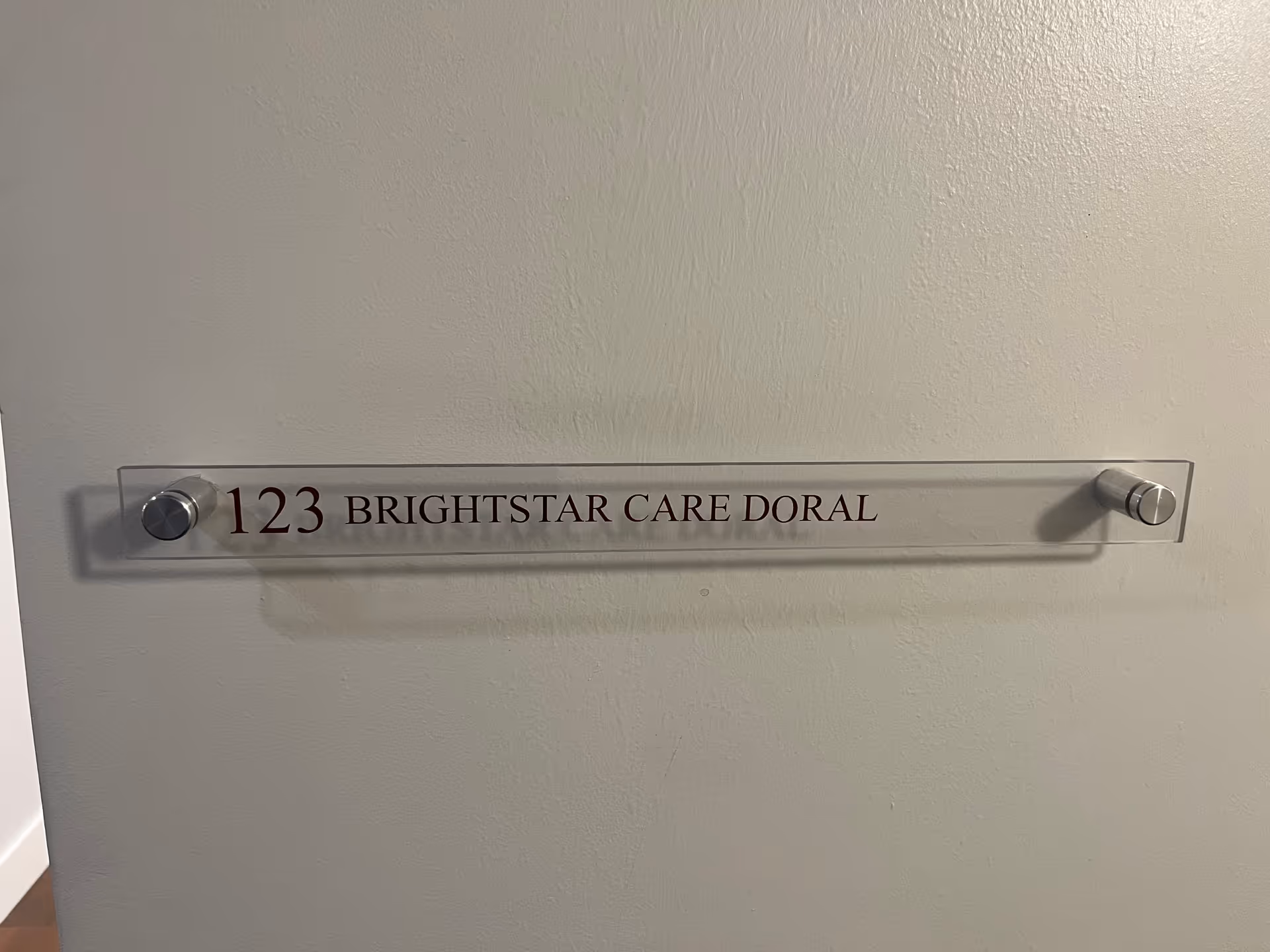 Clear acrylic wall sign displaying 123 BRIGHTSTAR CARE DORAL on a light wall.
