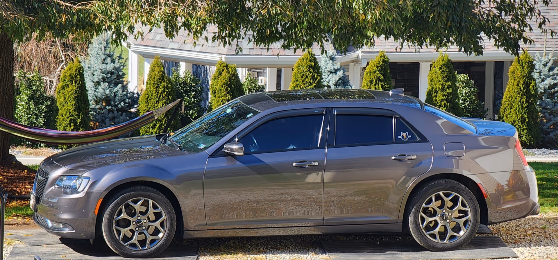 Gray sedan parked in front of a residential home with manicured shrubs and a hammock.