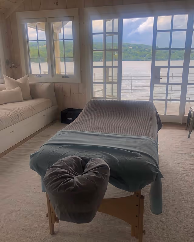 Bright interior treatment room with a massage table and lakeside view.