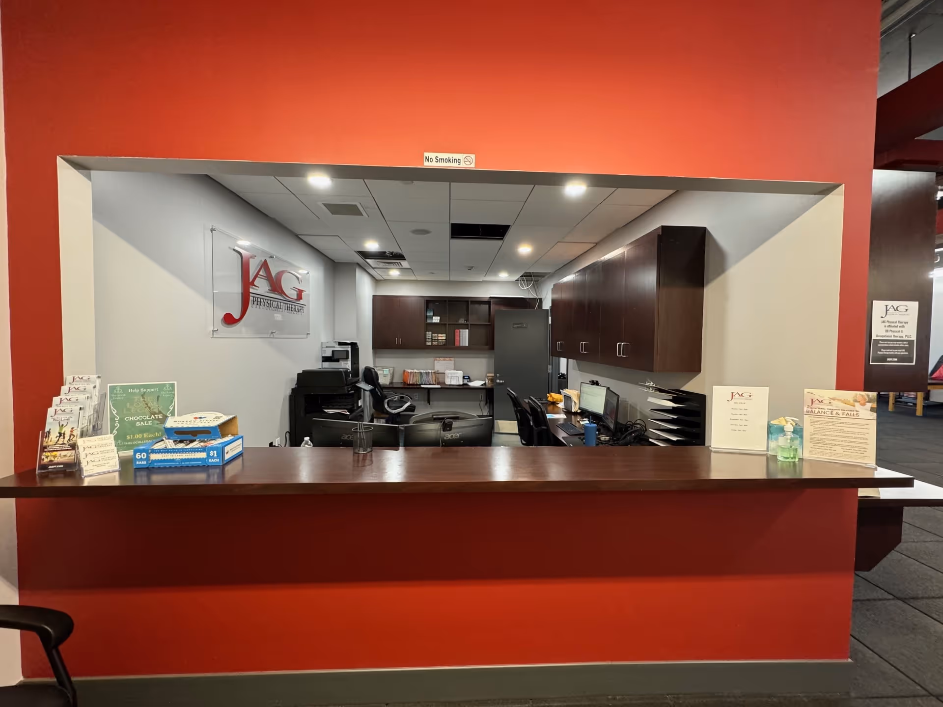 Red-walled reception area with a front desk, cabinets, and JAG Physical Therapy signage.