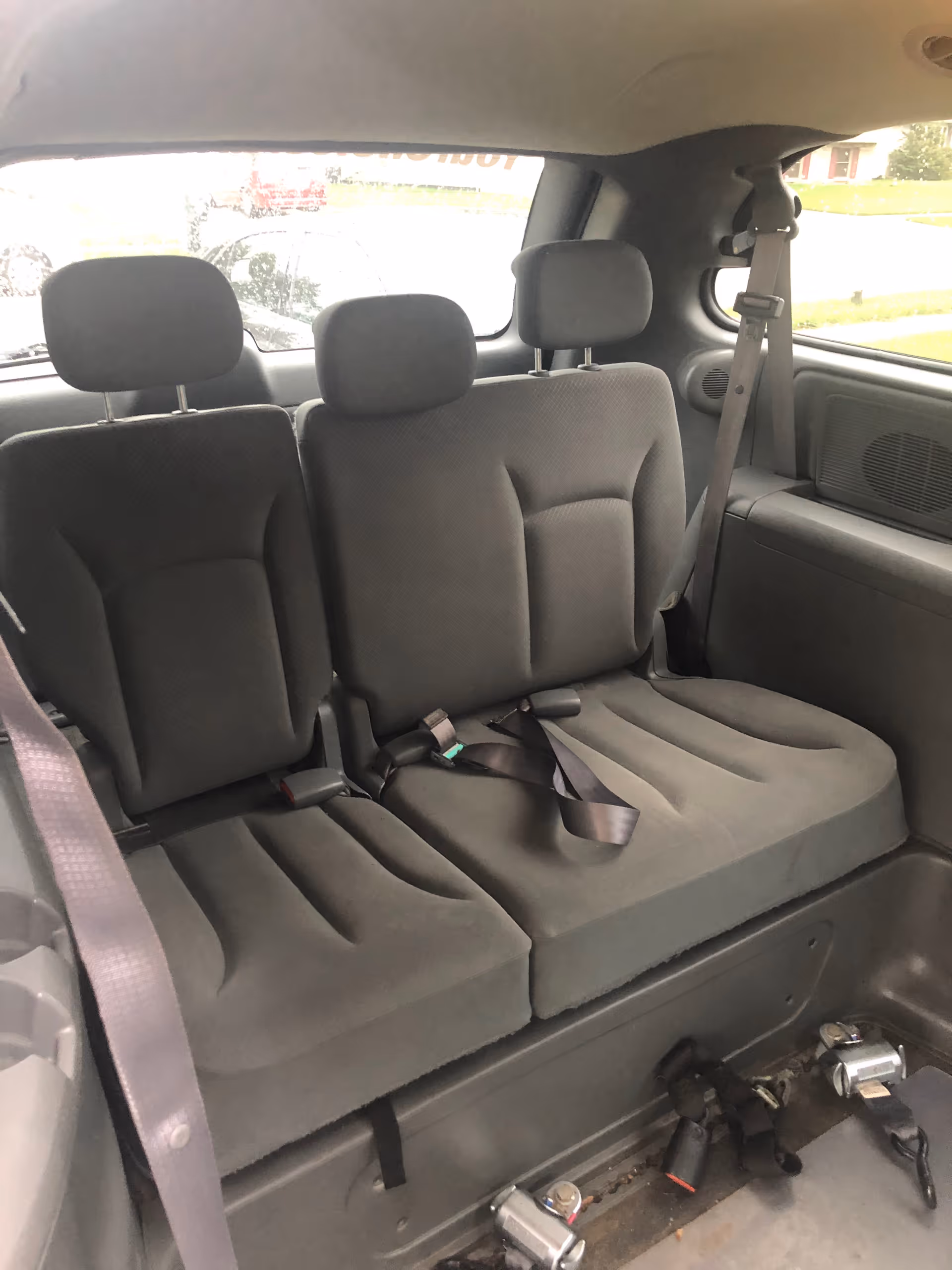 Rear row of gray car seats with seat belts inside a vehicle.