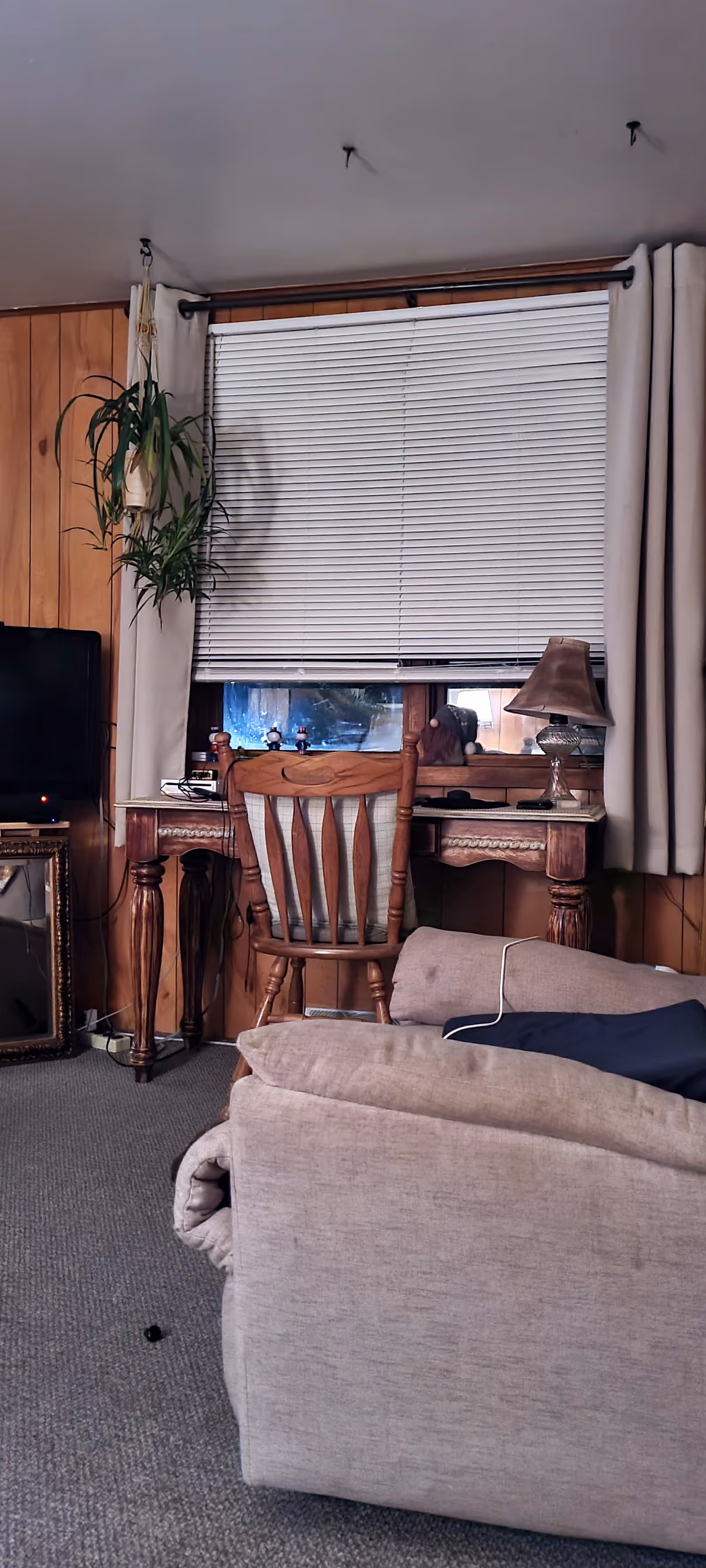 Cozy living room with a beige sofa, wooden desk by window blinds, and a plant.