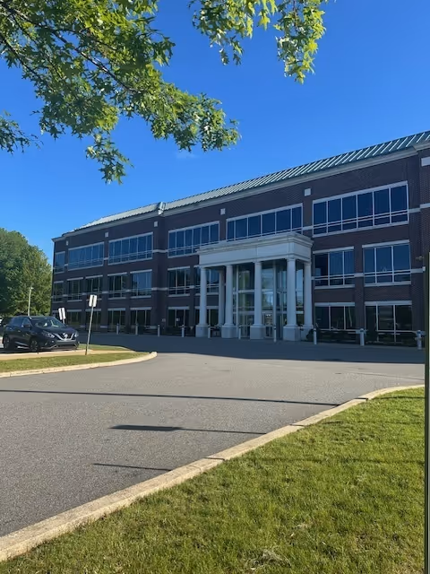 Exterior view of a brick, multi-story facility with glass entrance and surrounding lawn.