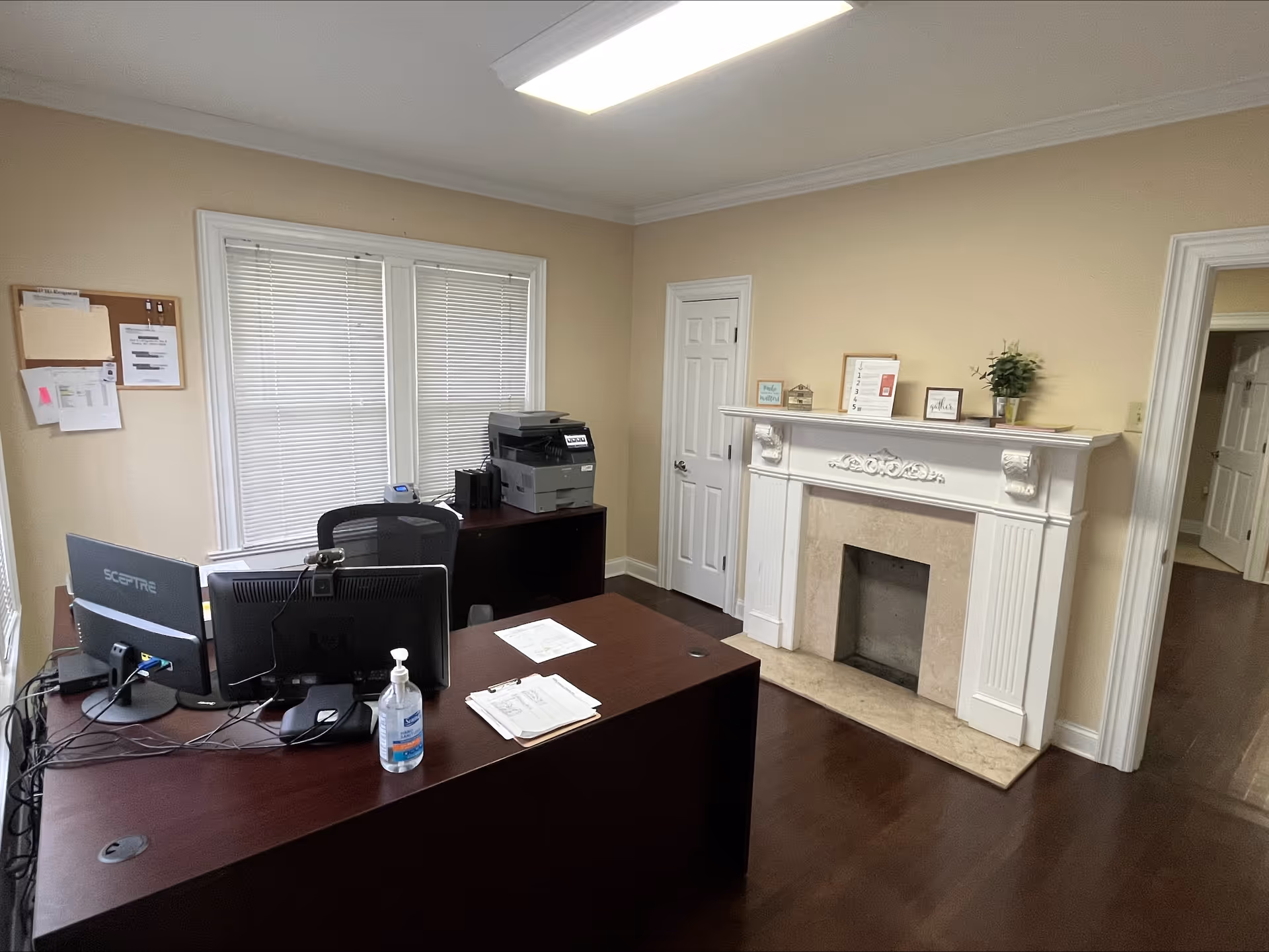 Office desk area with computers, printer, and a decorative fireplace mantel.