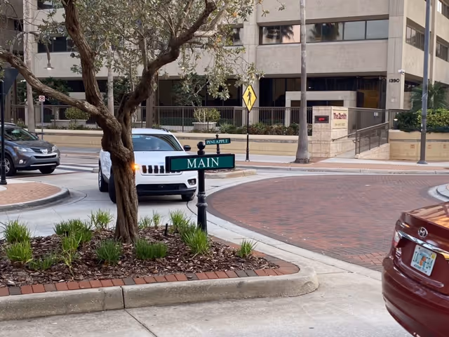 City street scene in front of a modern building with a car and greenery.