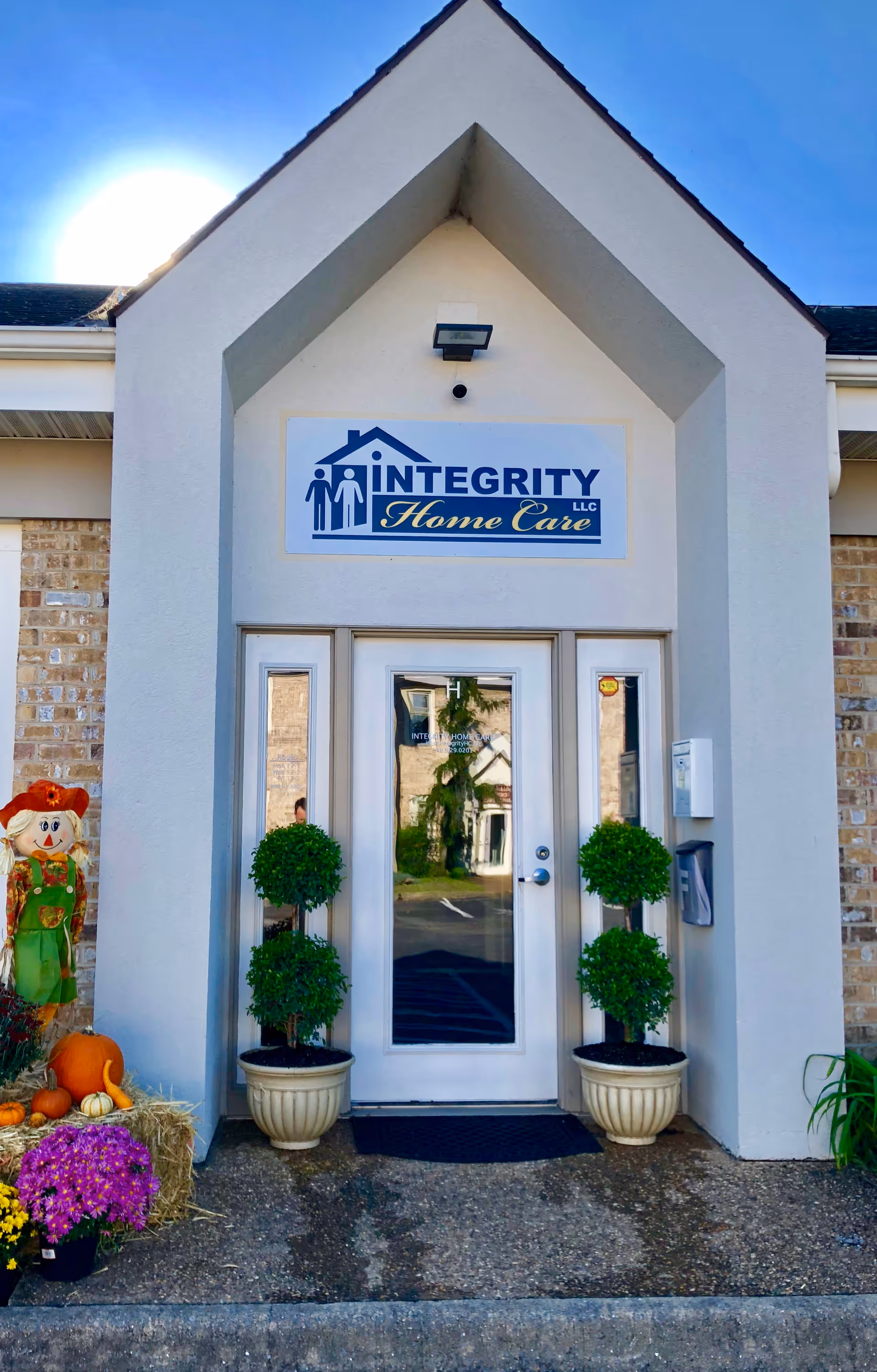 Front entrance of Integrity Home Care LLC with glass doors, potted shrubs, and pumpkins.
