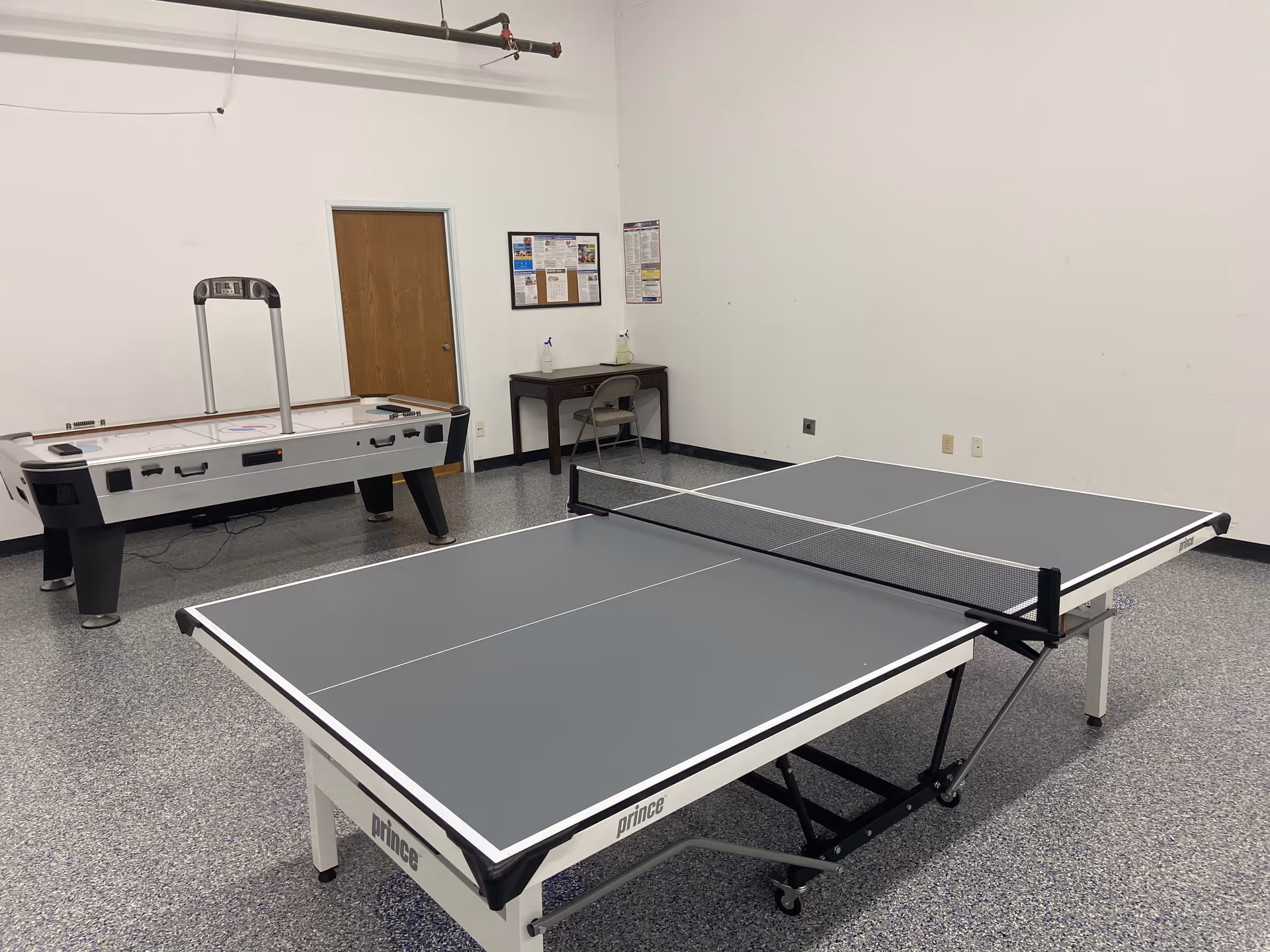 Recreation room with ping-pong and air-hockey tables, bulletin board, and a door.