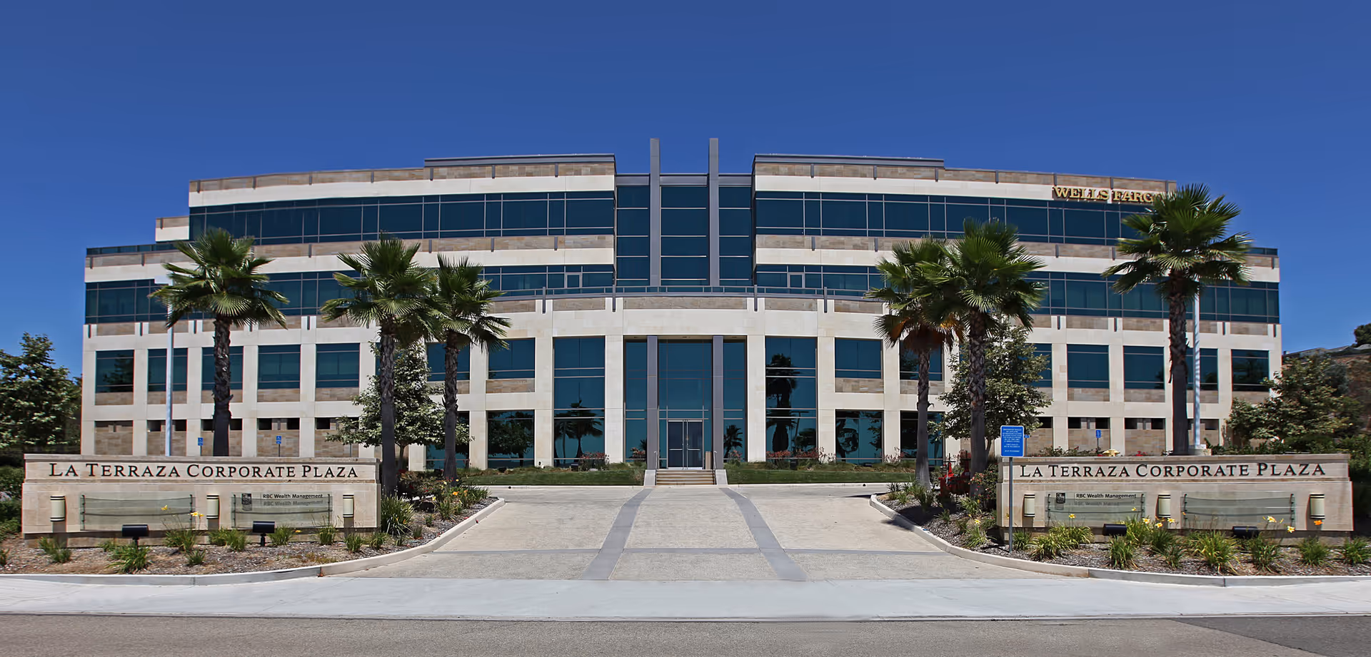 Exterior view of a modern office building with palm trees and stone signage columns.