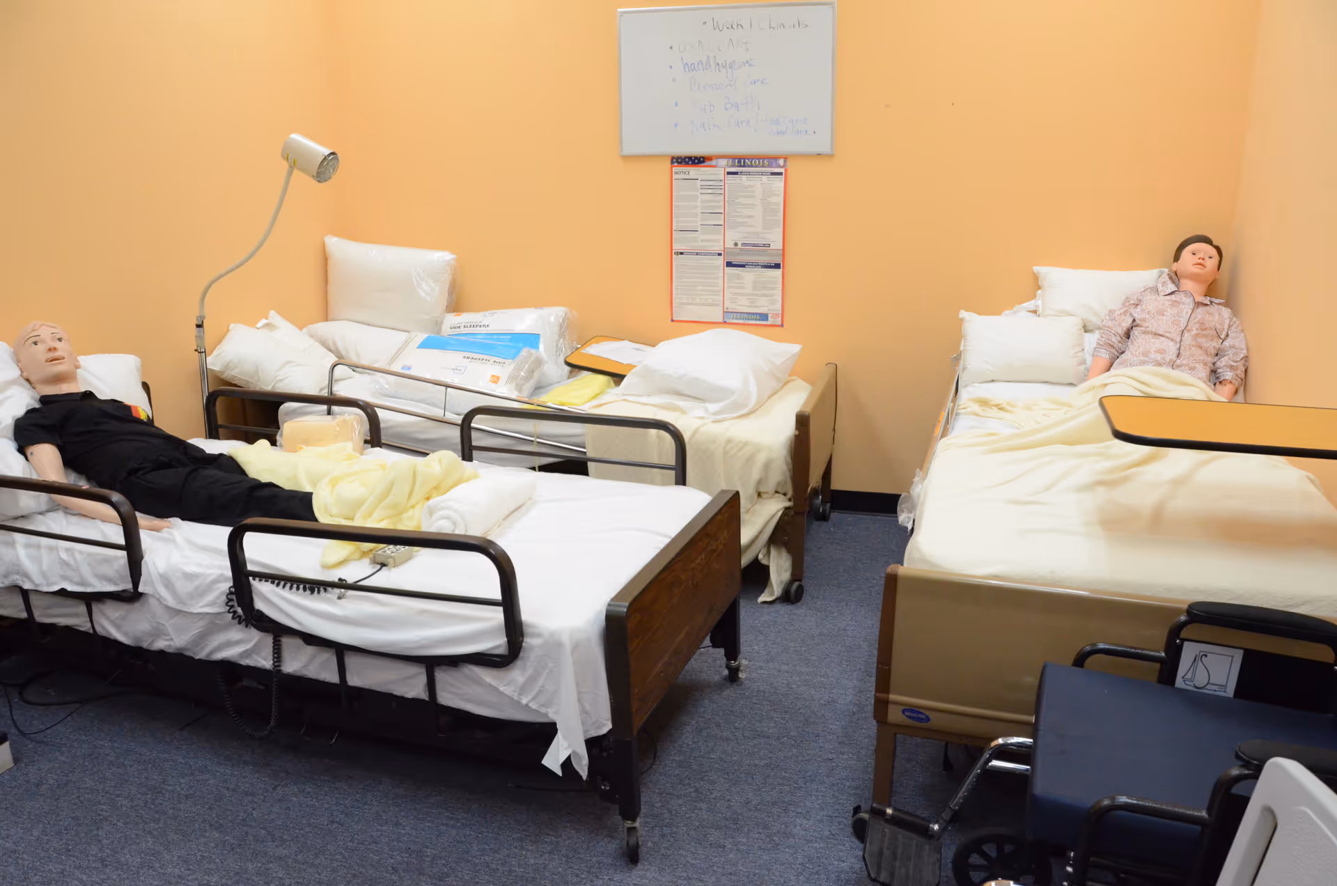 Two hospital beds with life-size mannequins lie in a peach-colored nursing training room.