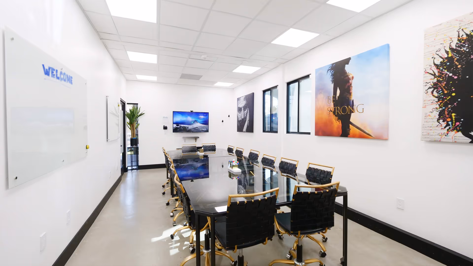 A conference room with a long glass table, black chairs, and art on white walls.