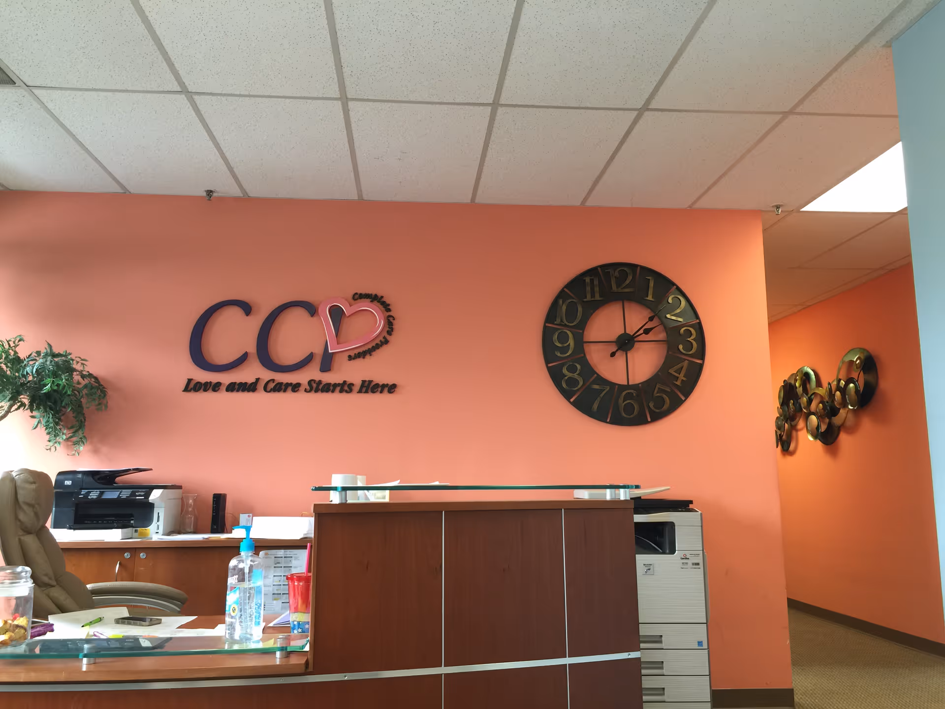 Reception desk in a peach lobby with a CC logo, large clock, and office equipment.