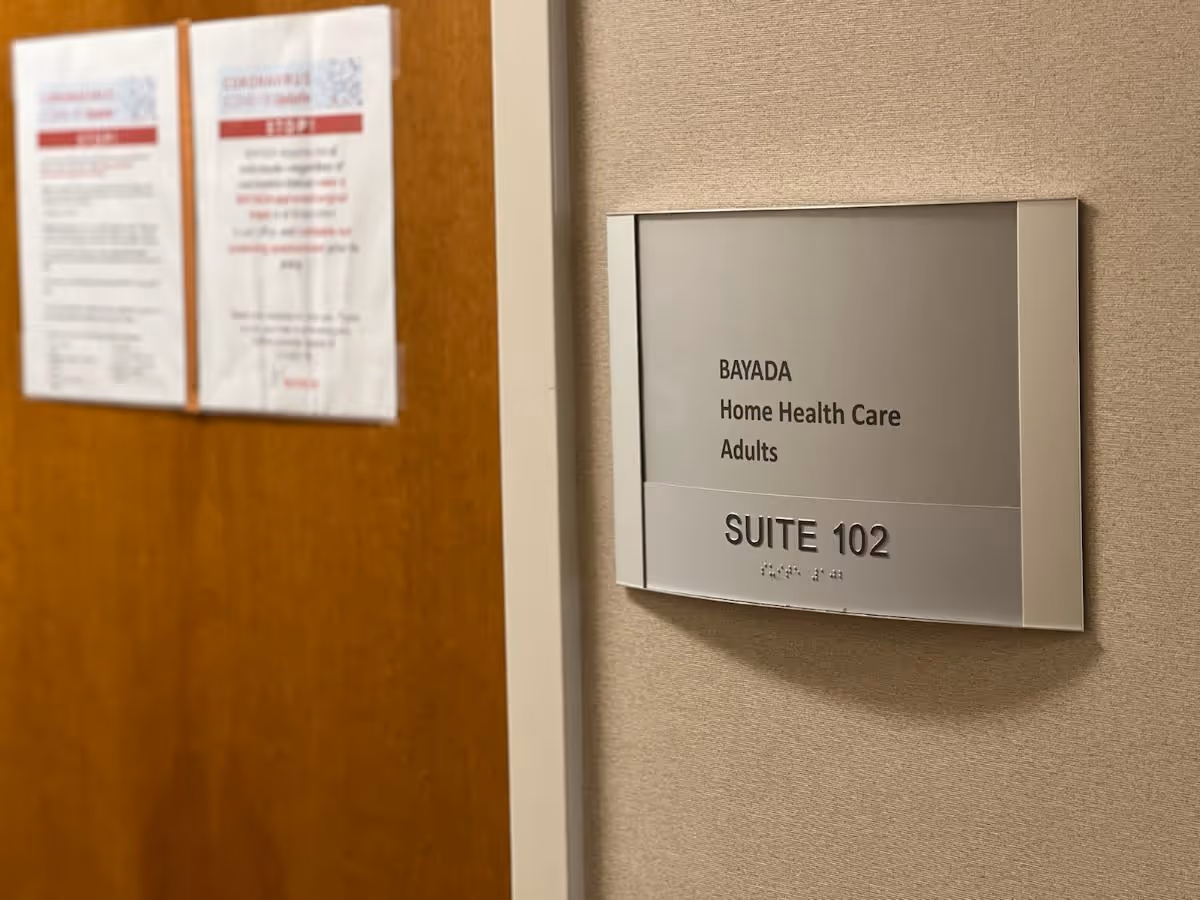 Close-up of BAYADA suite sign on beige hallway wall inside a facility.