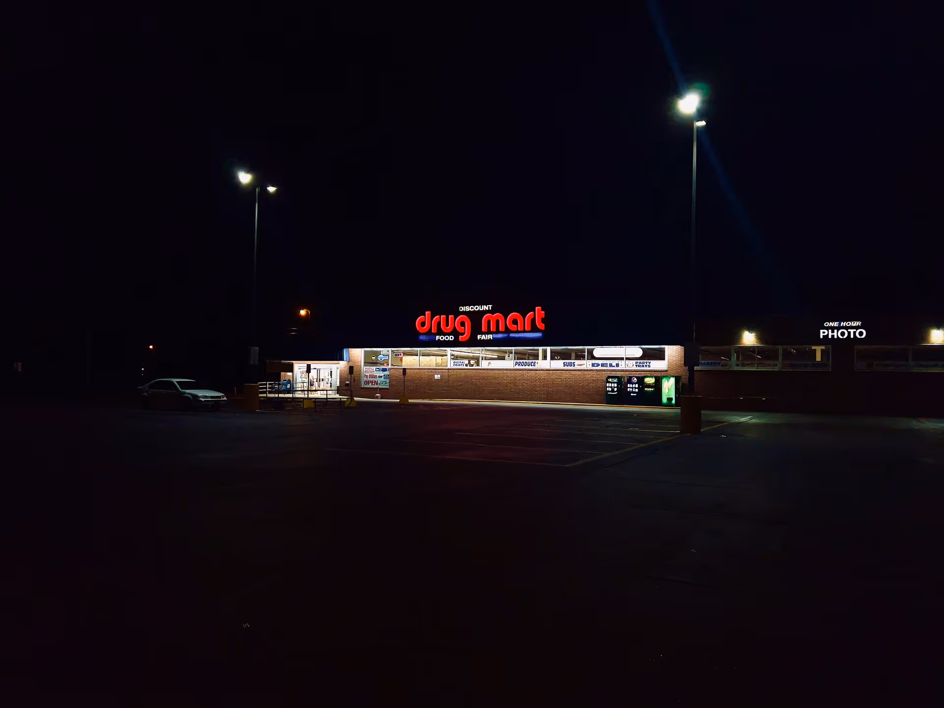 Night view of Discount Drug Mart storefront with bright sign and empty parking lot