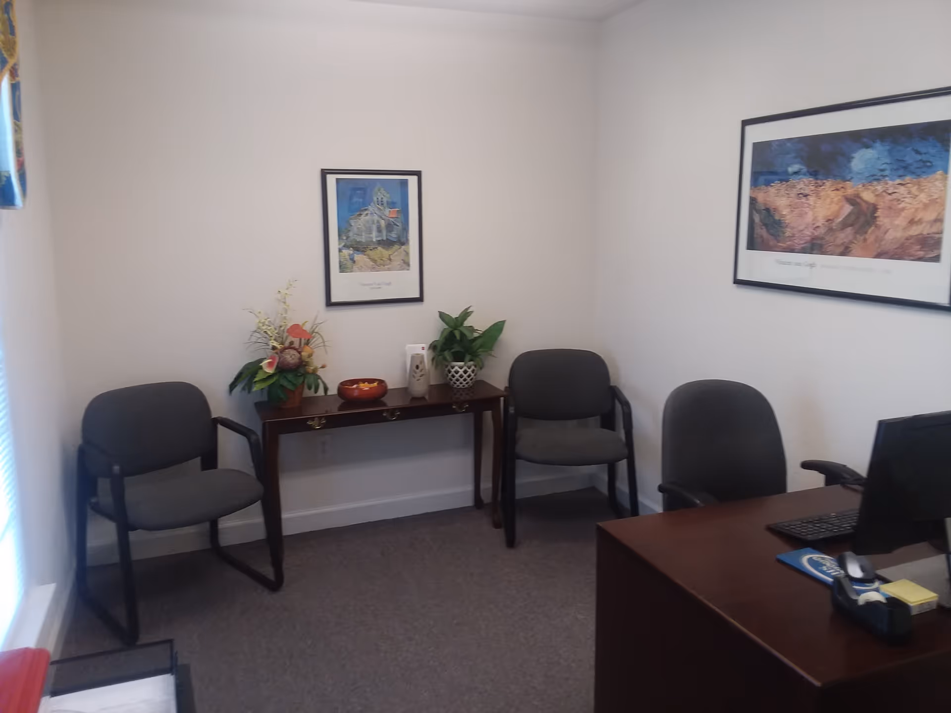 Small office waiting area in a senior facility with chairs, a desk, and wall art.