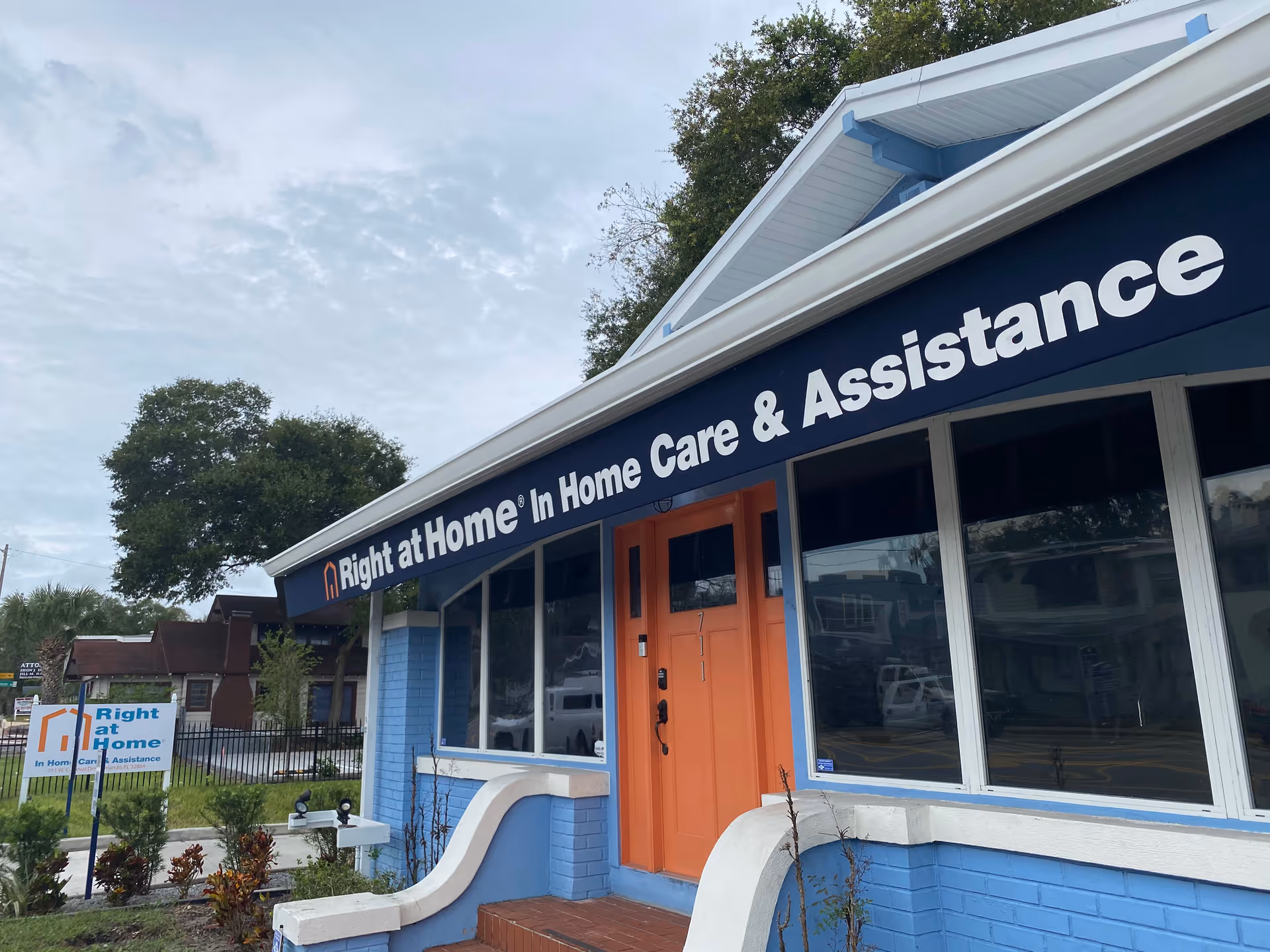 Exterior view of a blue building with orange door and a large Right at Home sign.