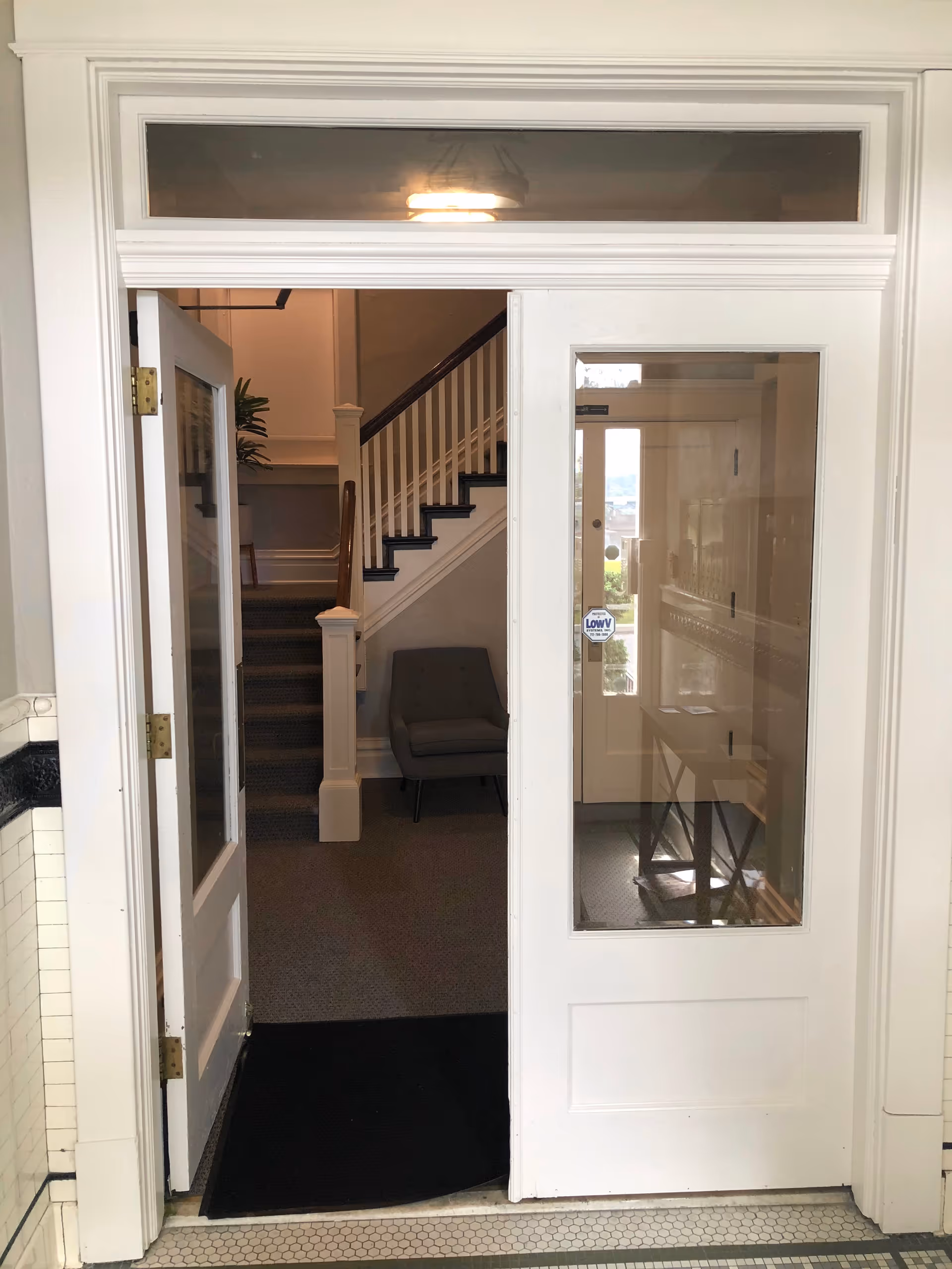 White interior doorway with glass panels opens to stairs and seating area.