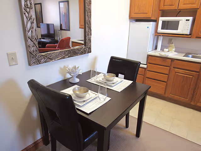 Dining table for two with place settings beside a kitchen area.