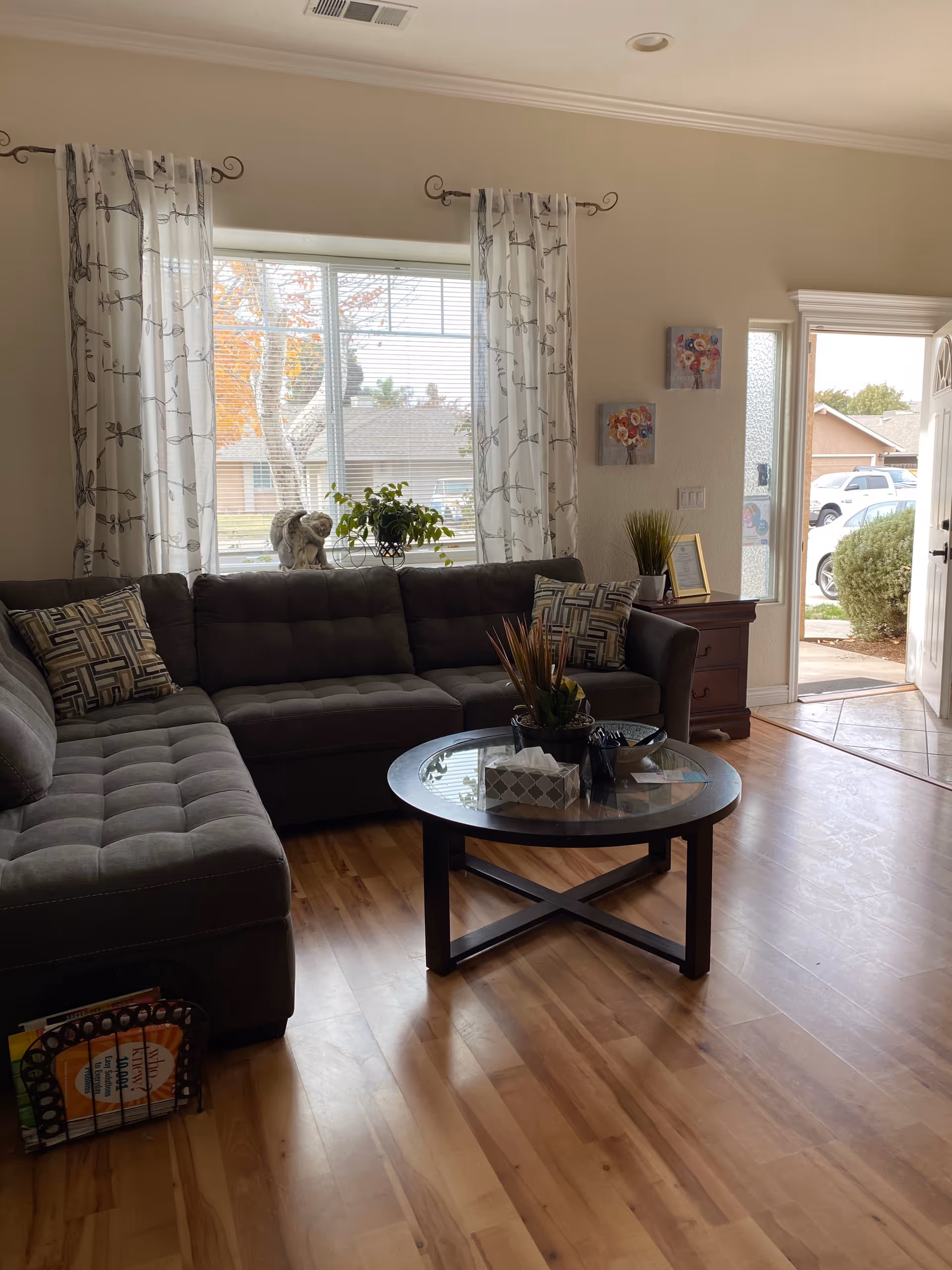 Cozy living room with gray sectional sofa, glass coffee table, and open door to outdoors.