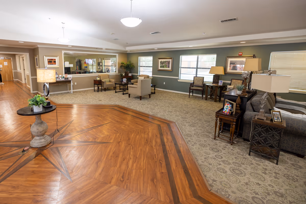 Spacious senior living common area with seating, lamps, and a star-patterned wooden floor.