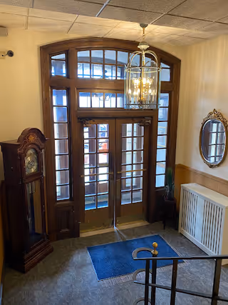 Elegant foyer entrance with wooden framed glass doors, chandelier, grandfather clock, and decorative mirror.