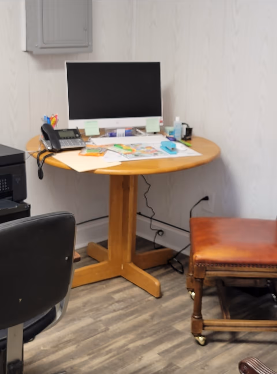 Office workspace with computer monitor, phone, documents on a round wooden desk.