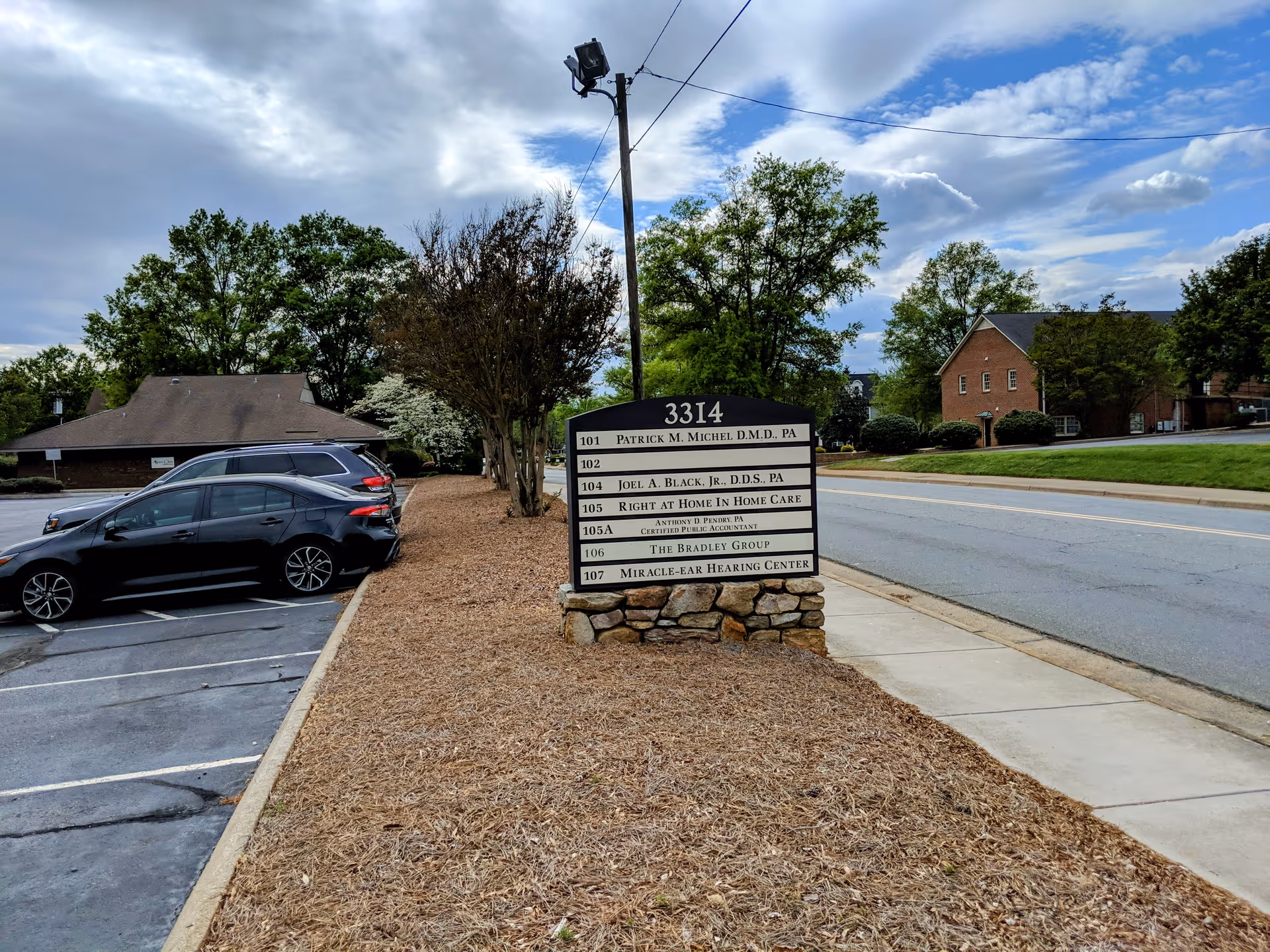A street view featuring a facility sign, parked cars, and a sidewalk.