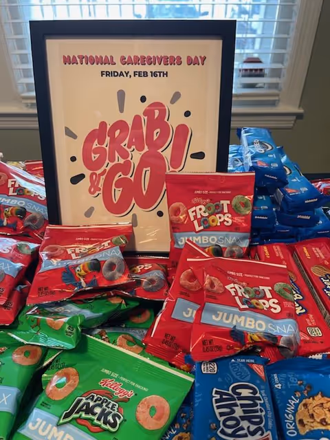 Framed National Caregivers Day poster on a table surrounded by colorful snack packages.