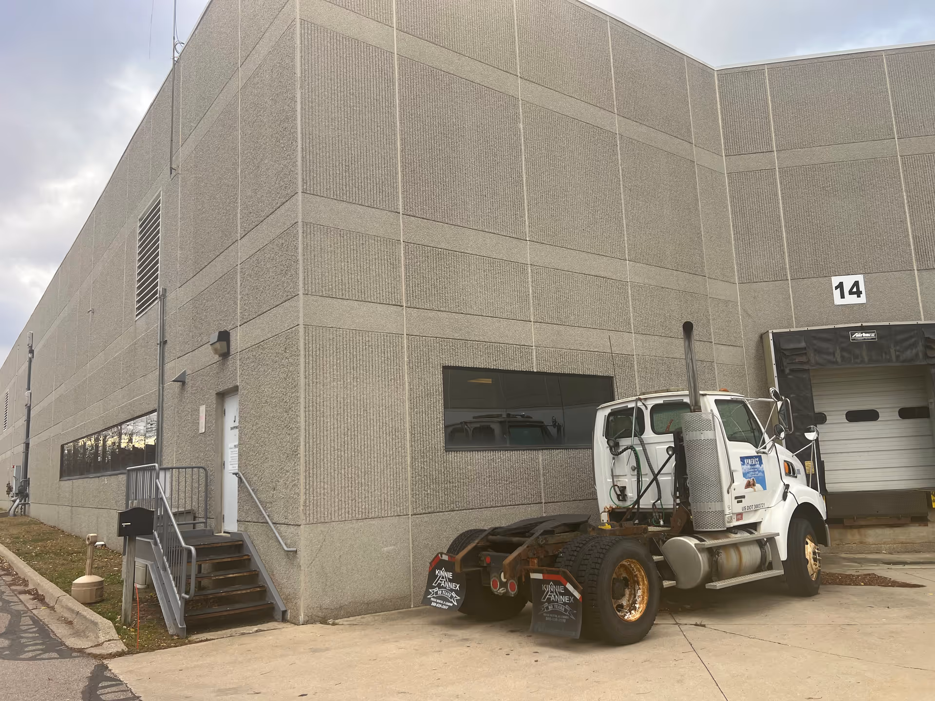 A gray industrial building exterior with a white truck parked by a loading dock.