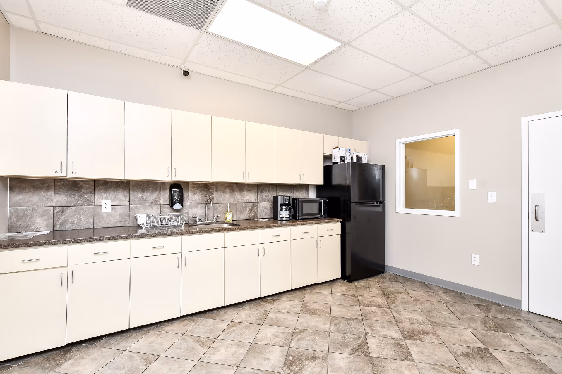 Clean kitchenette with white cabinets, counter, sink, and a black refrigerator