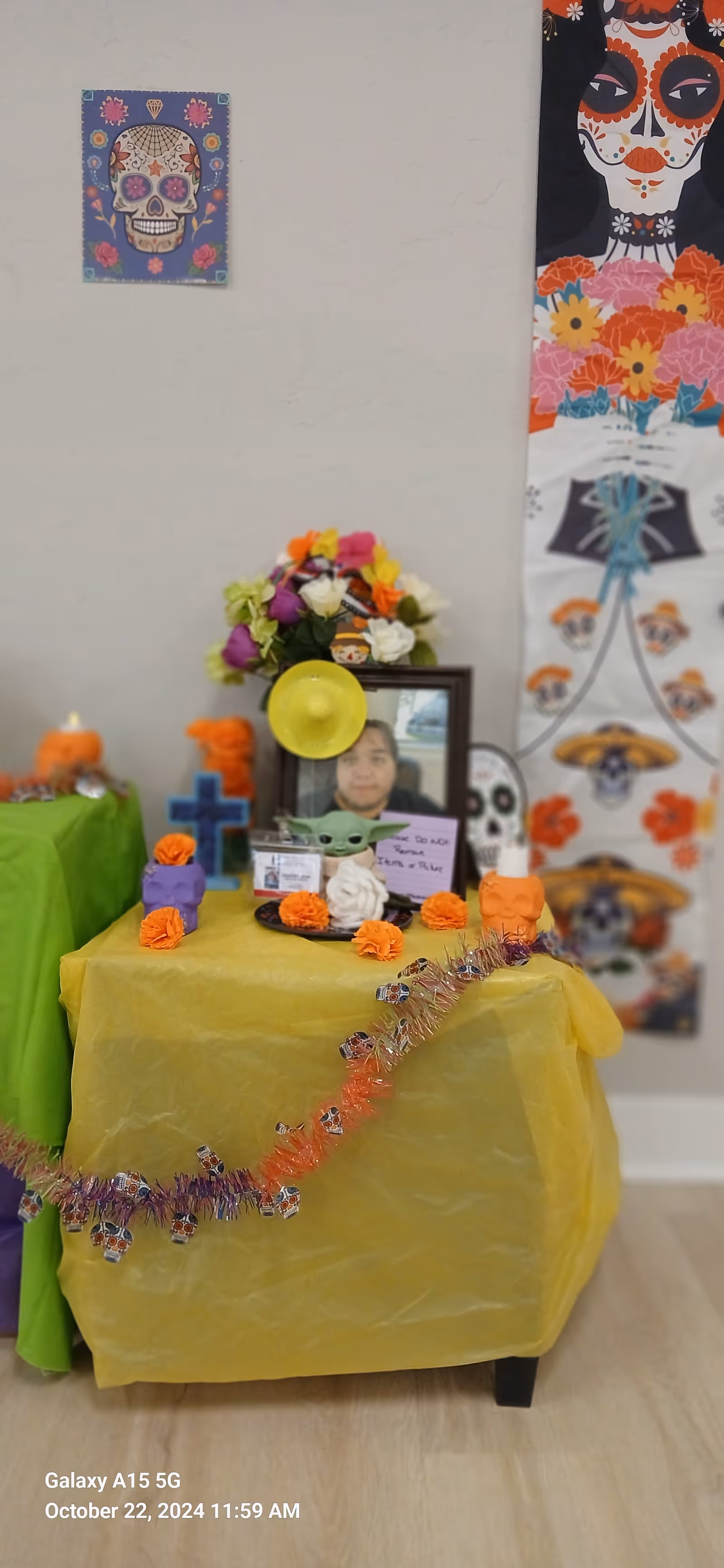 Colorful Day of the Dead altar arranged on a yellow-draped table inside a room.