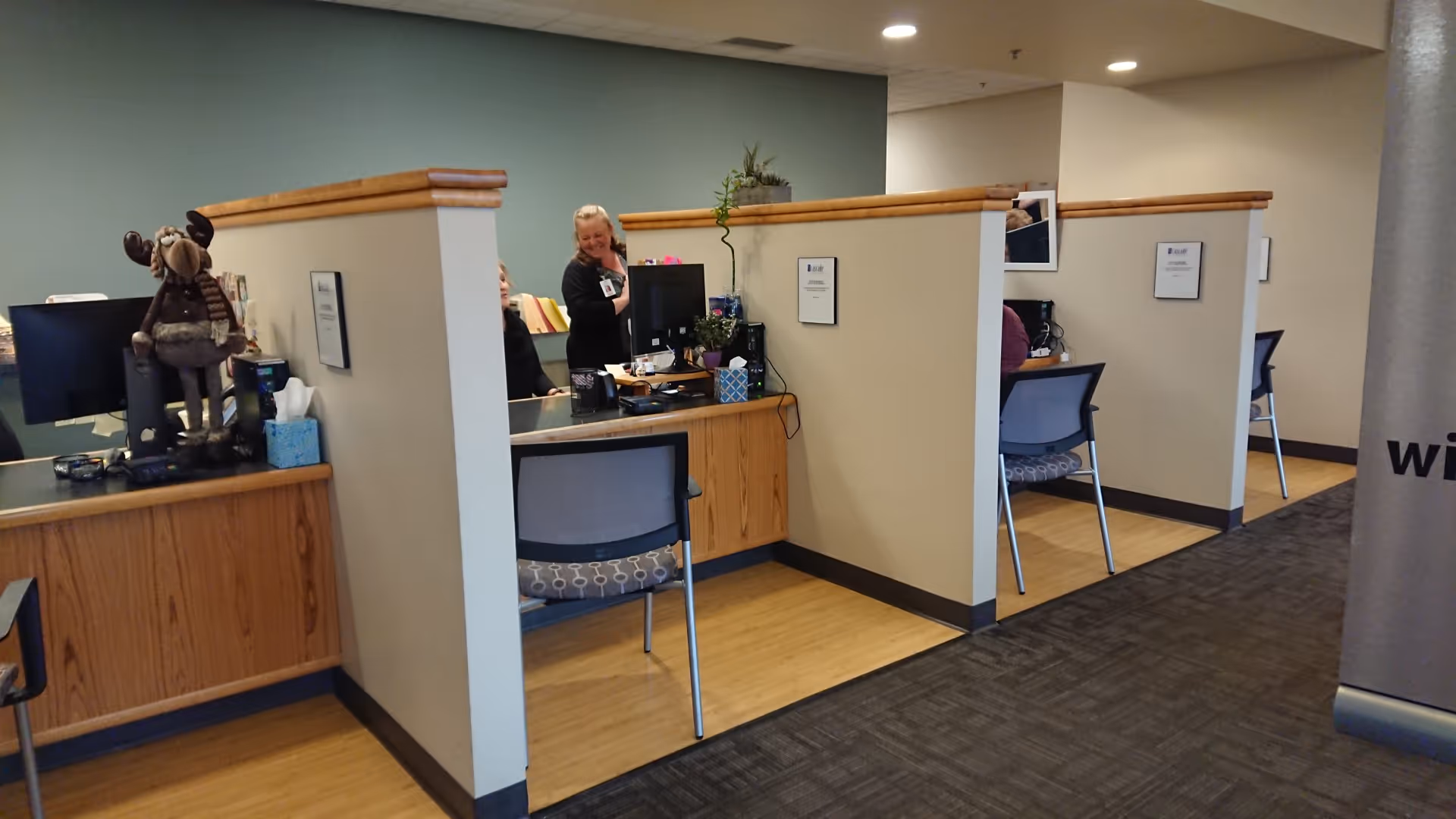 Reception area with partitioned cubicles, desks, computers, and staff inside a senior living facility.