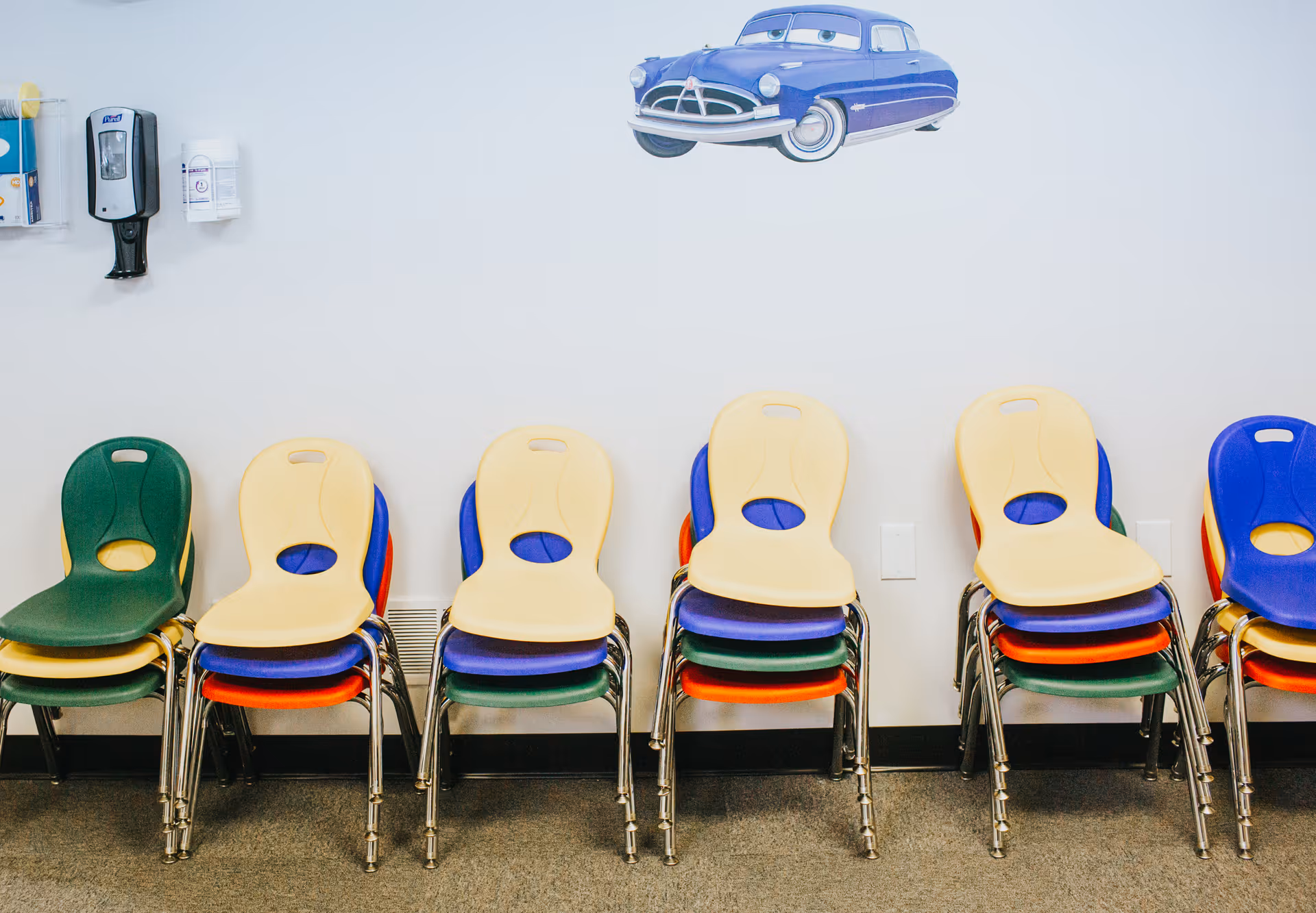 Colorful plastic chairs stacked along a pale interior wall with a blue car mural above.