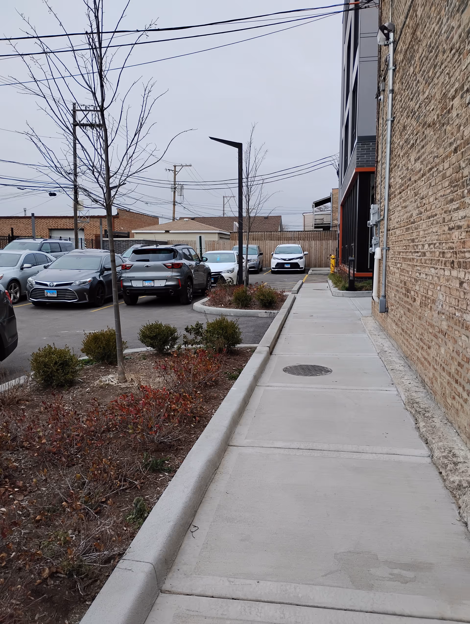 Exterior view of a brick building with a sidewalk and parked cars in a lot.