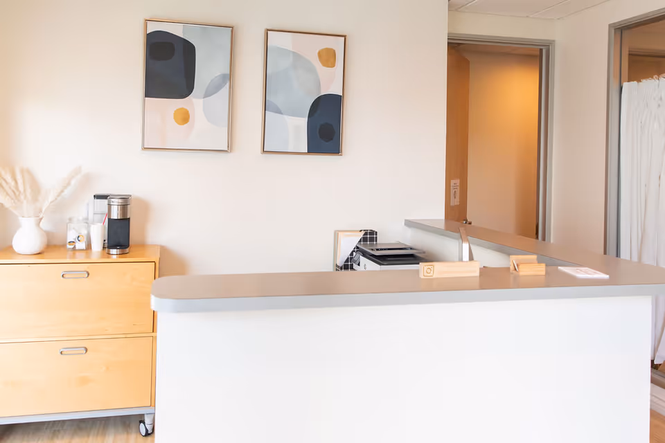 Curved reception counter overlooks a bright interior with abstract wall art and a coffee station.