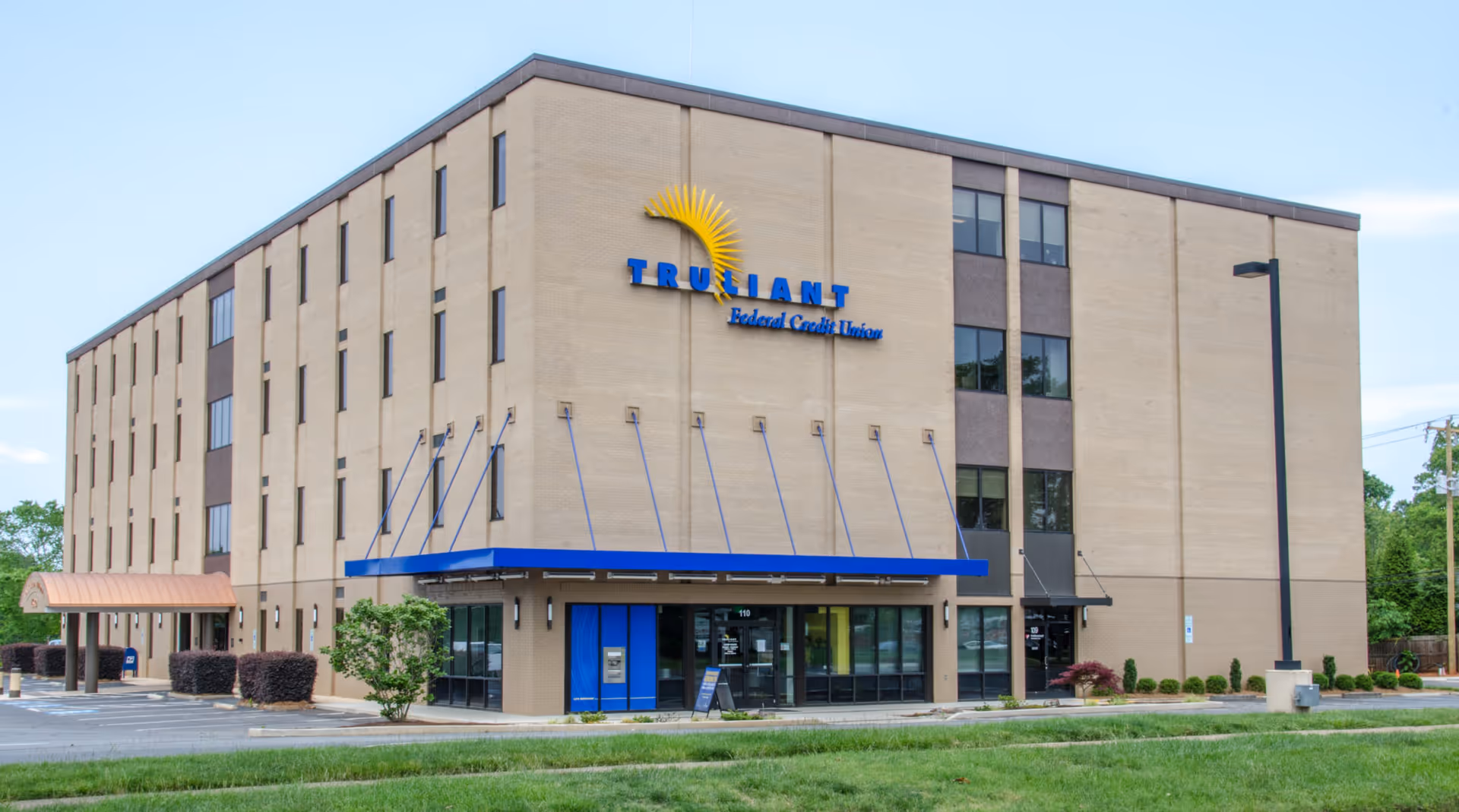 Exterior view of a beige multi-story building with a blue entrance awning and landscaping.