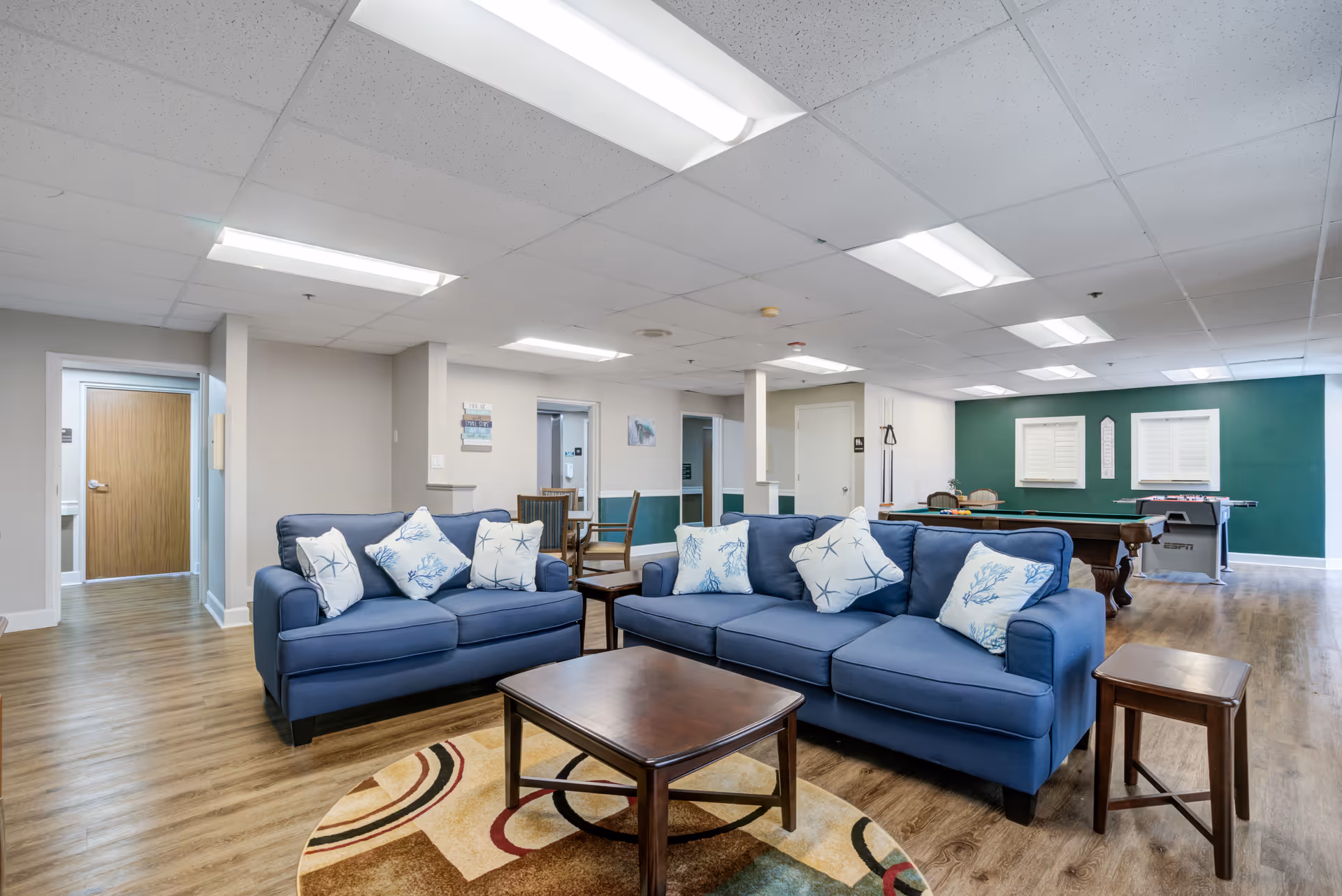 Spacious indoor living area with blue couches, coffee tables, and a pool table.