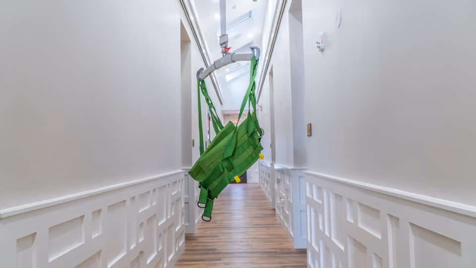 Long white hallway with wainscoting and a green evacuation chair suspended from the ceiling.