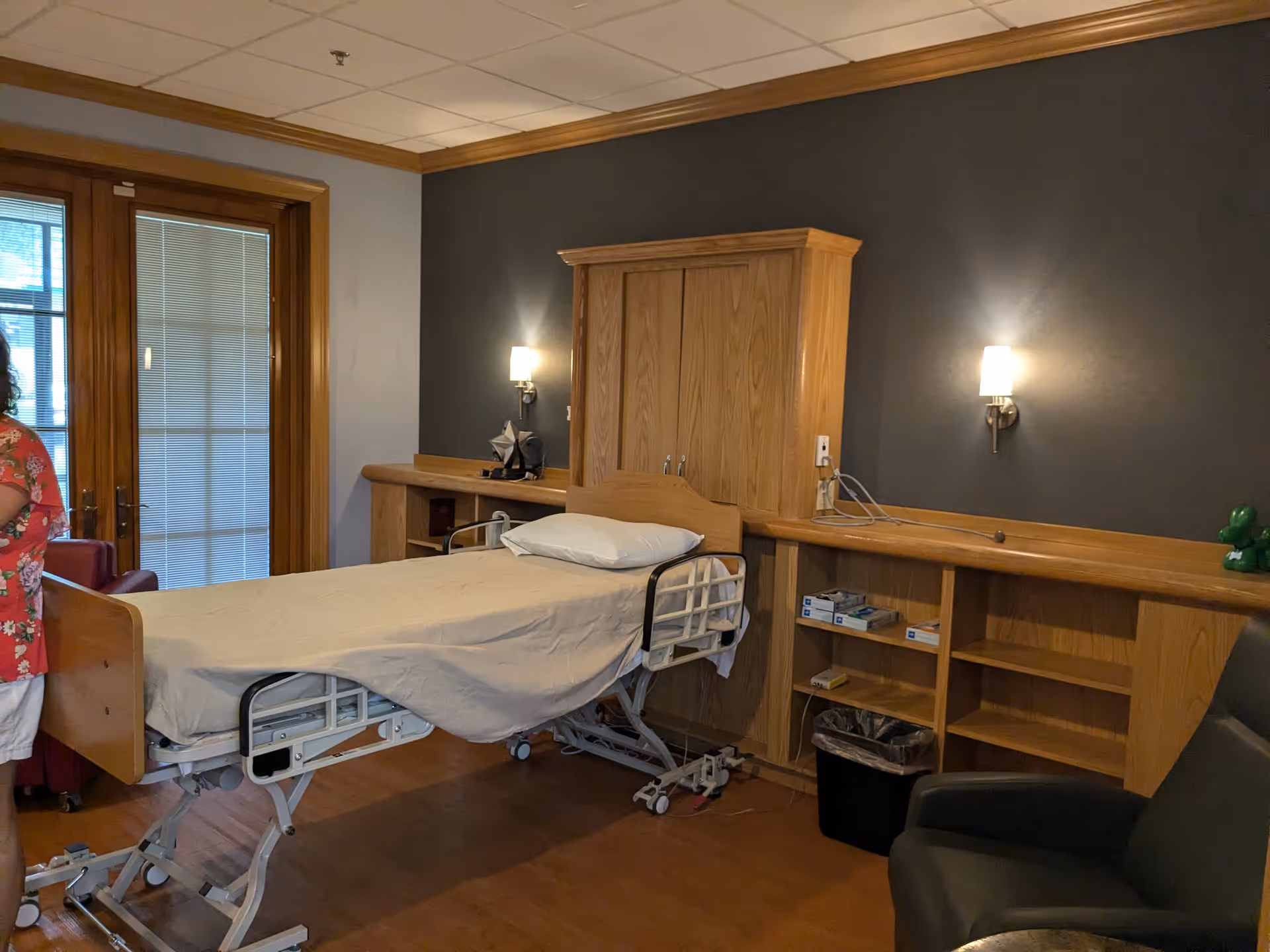 Hospice patient room with a hospital bed, wooden cabinetry, and seating.
