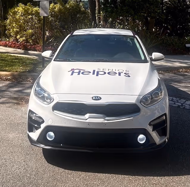White Kia SUV with Senior Helpers logo parked on a street.