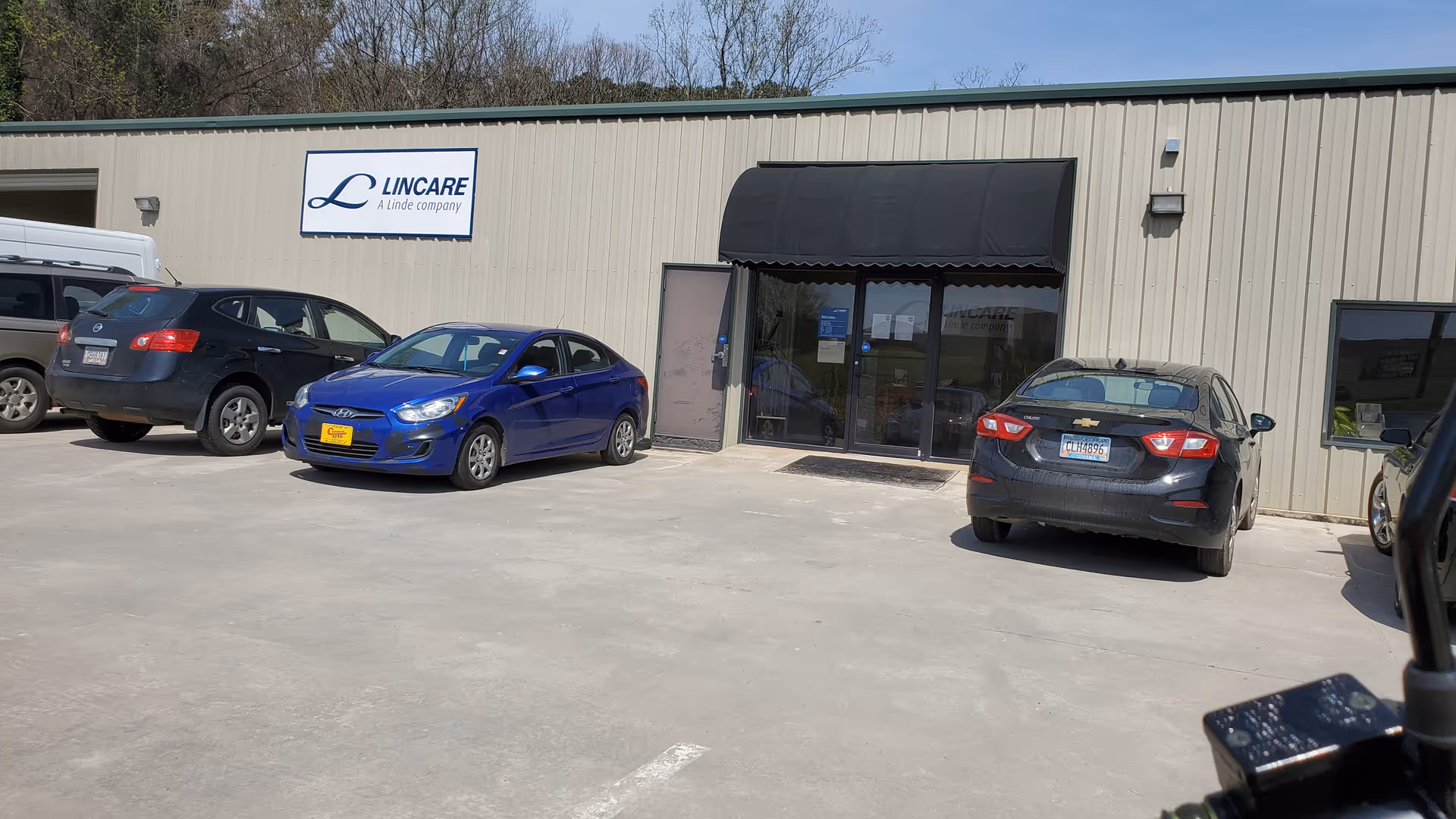 Exterior view of LINCARE facility with sign, awning, and parked cars at the entrance.