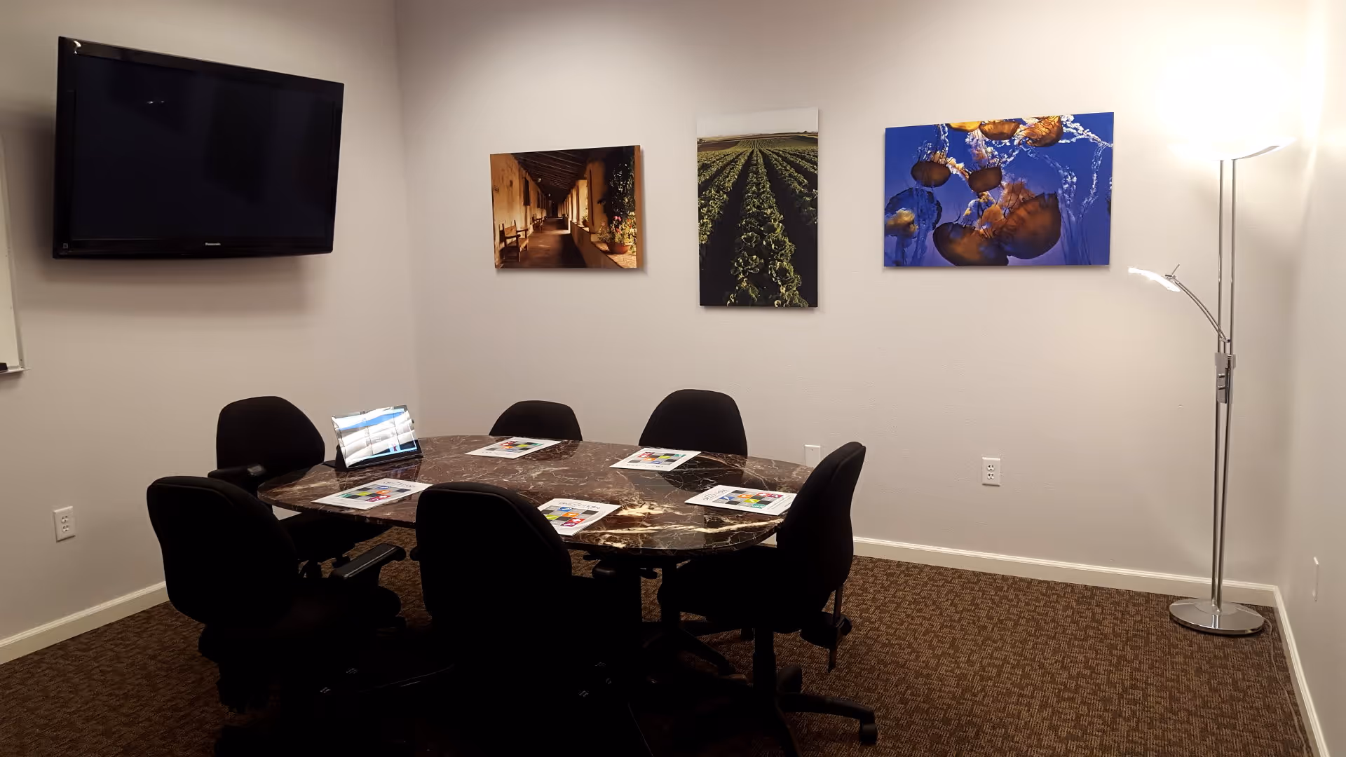 Conference room with marble table, black chairs, wall art, TV, and floor lamp.