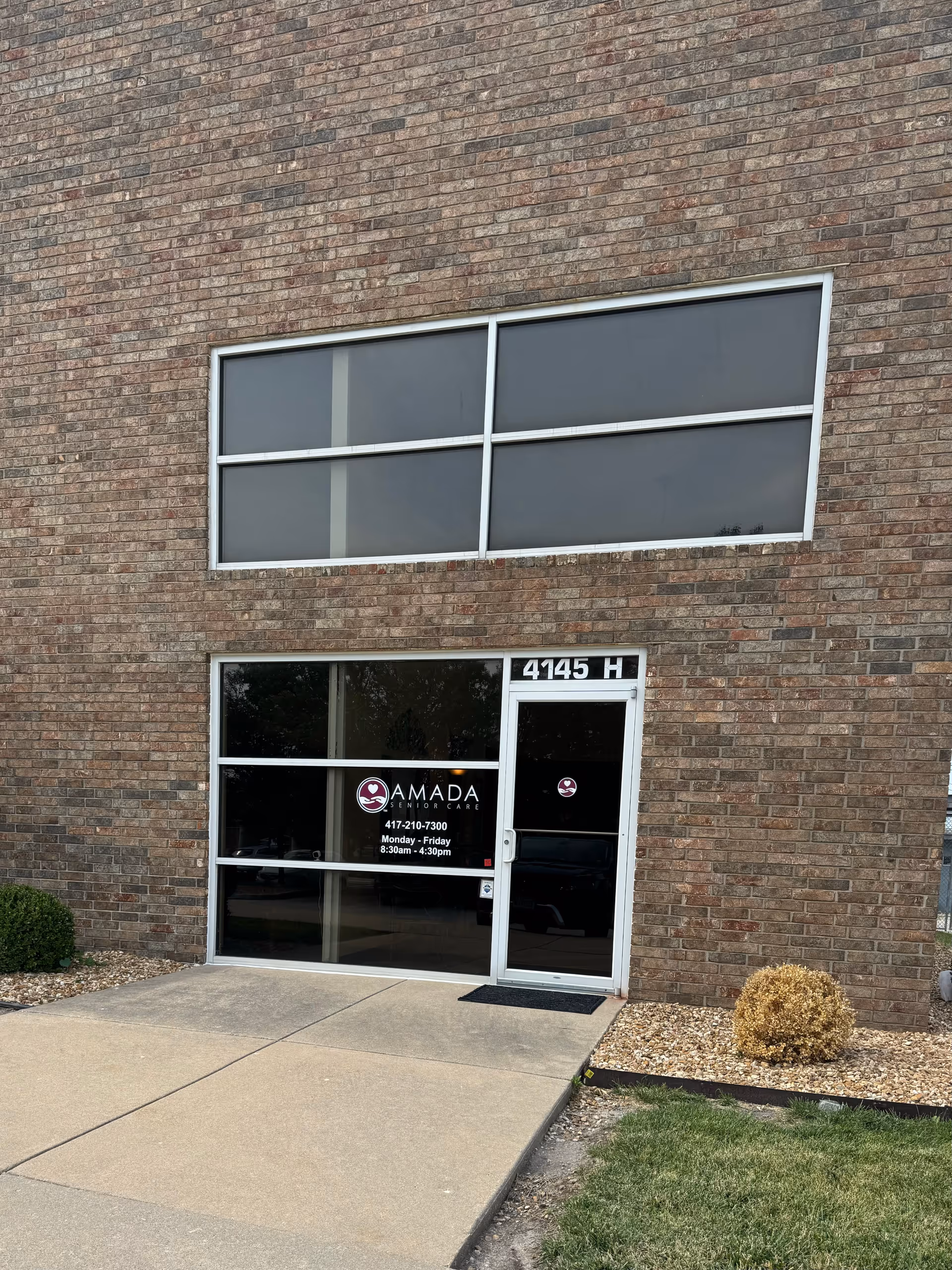 Brick building exterior with large front windows and Amada Senior Care entrance.