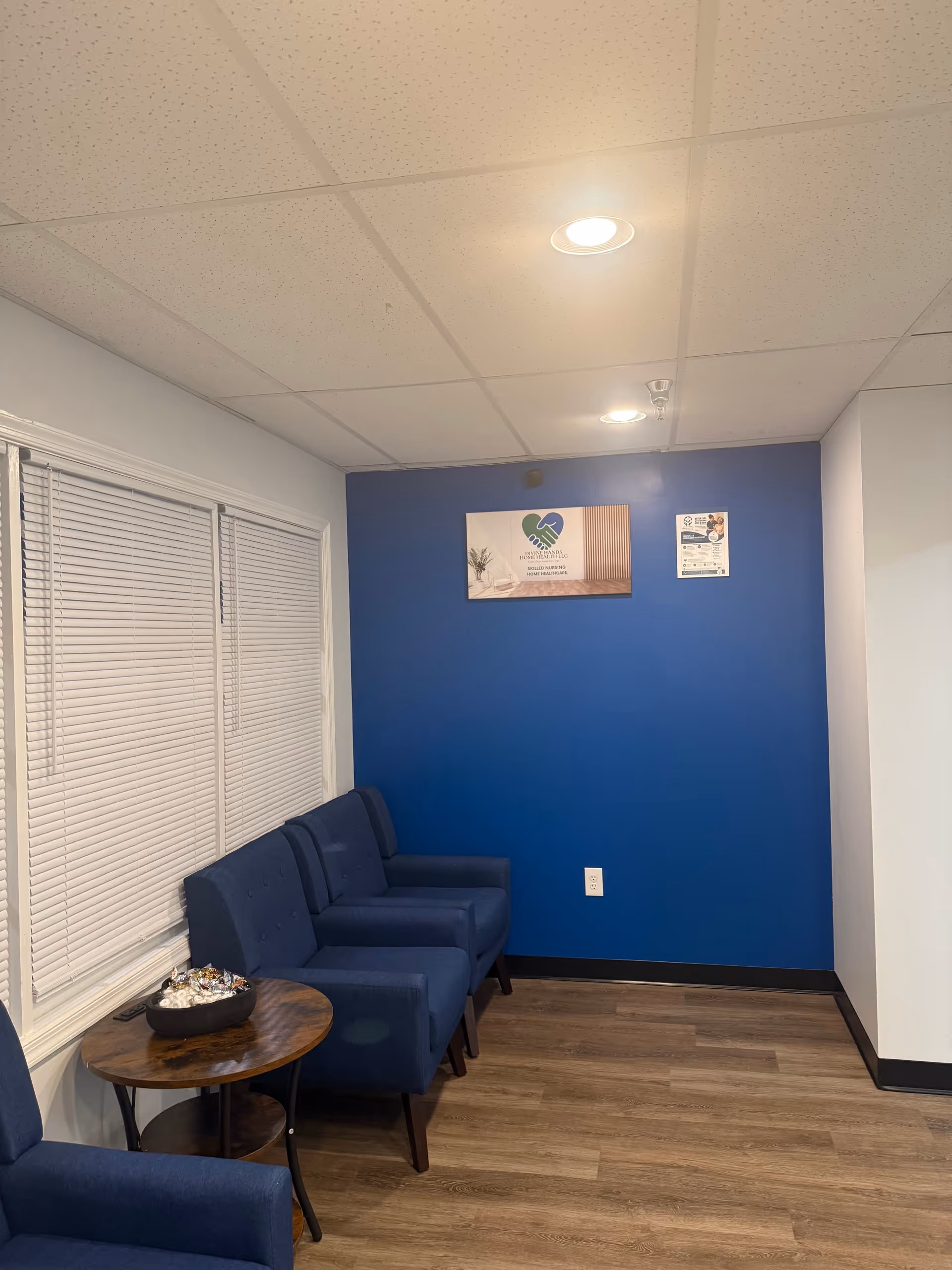 Blue-walled waiting area with blue chairs along the wall and a small round table.