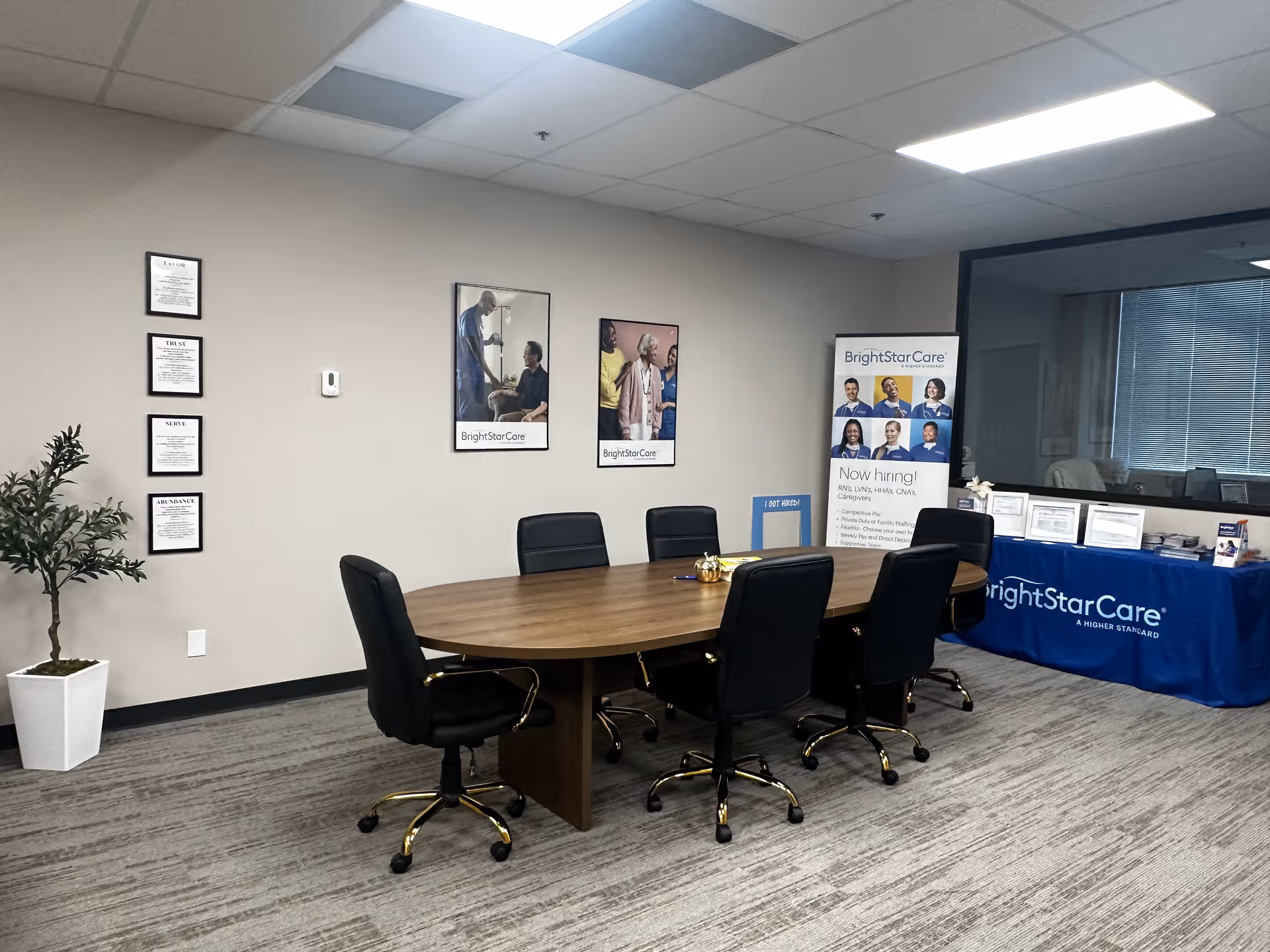 A BrightStarCare conference room with an oval table, black chairs, posters, and a banner.