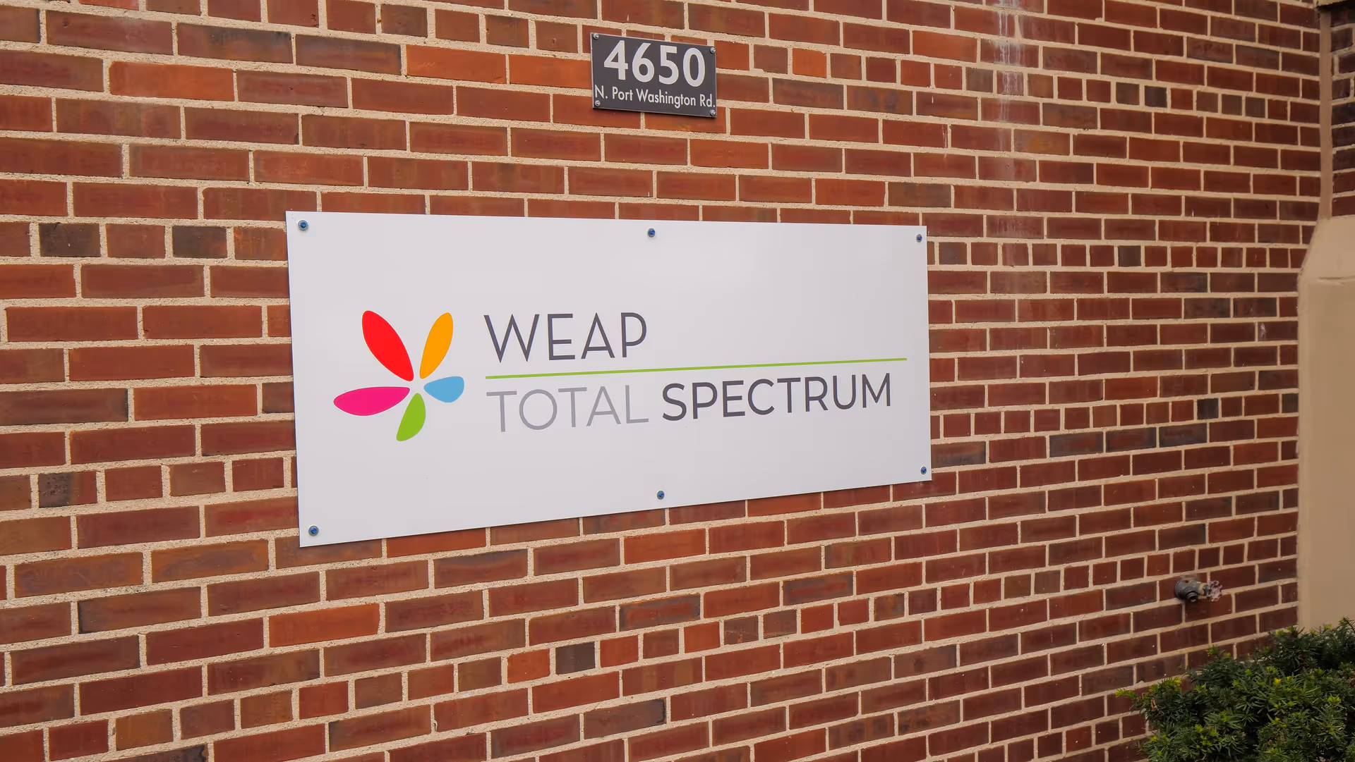 Brick exterior wall with a WEAP Total Spectrum sign and 4650 address plaque