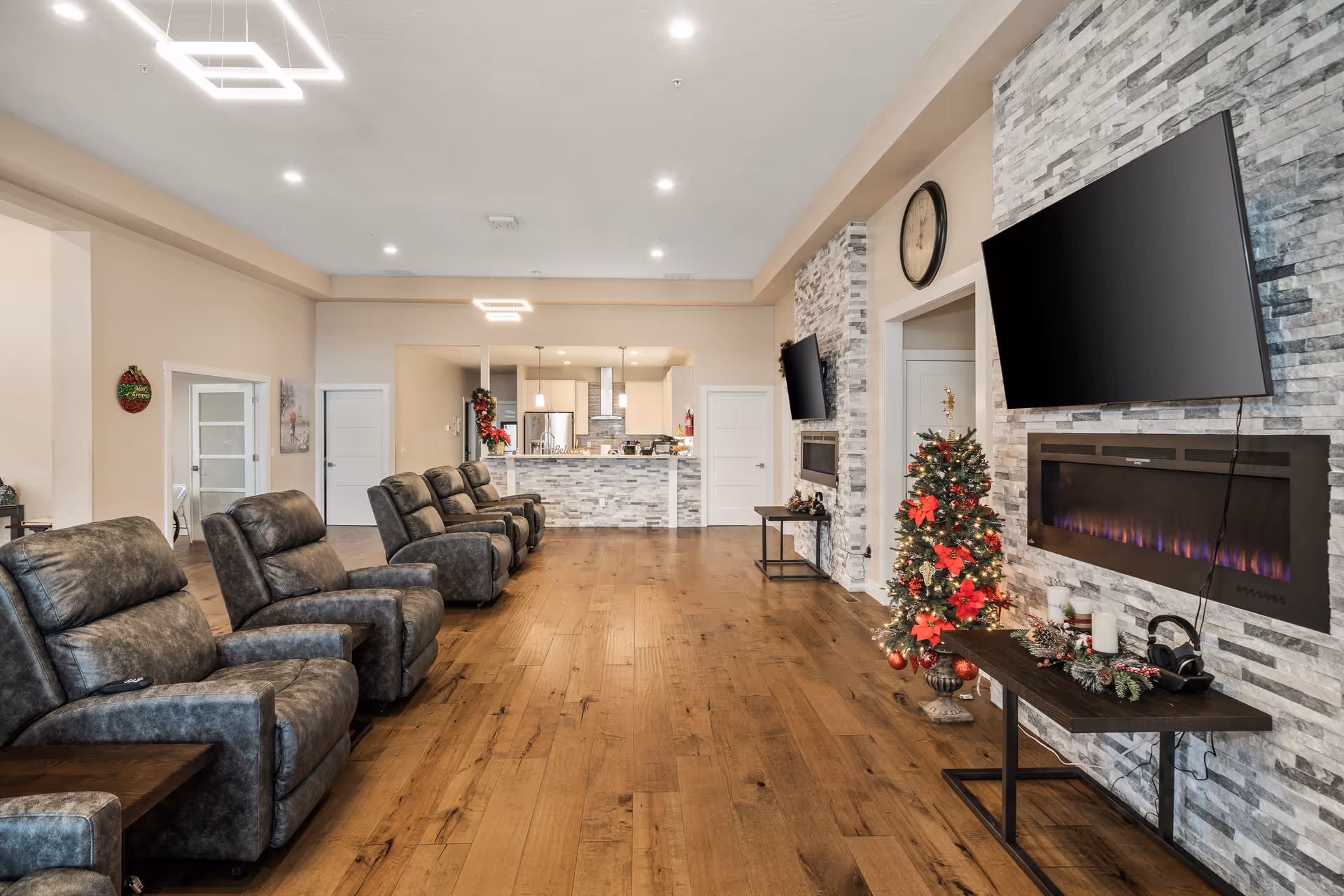 Spacious senior living room with recliners, fireplace, Christmas tree, and wall-mounted TV.