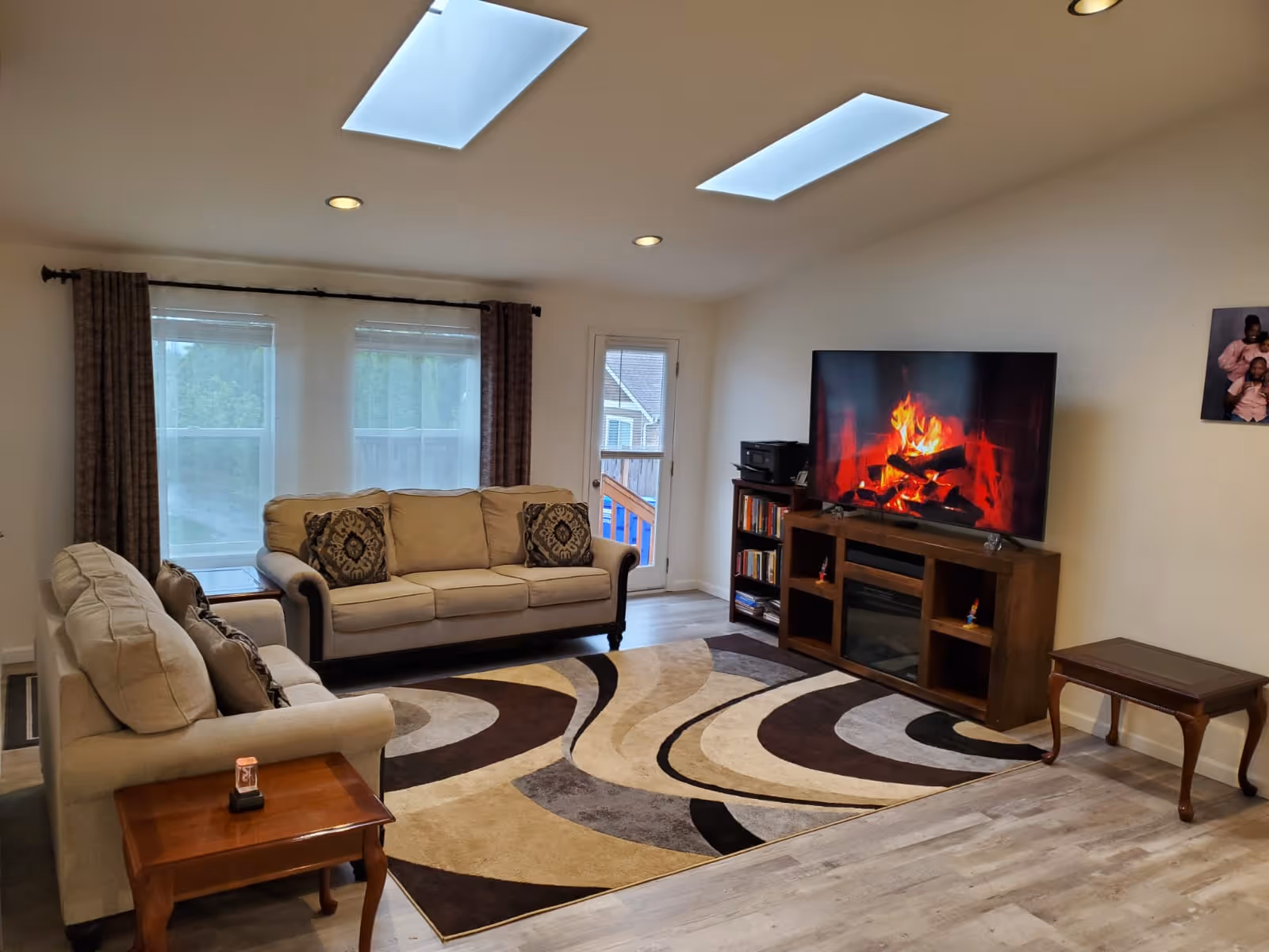 Cozy living room with beige couches, a rug, TV, and skylights in a senior living facility.