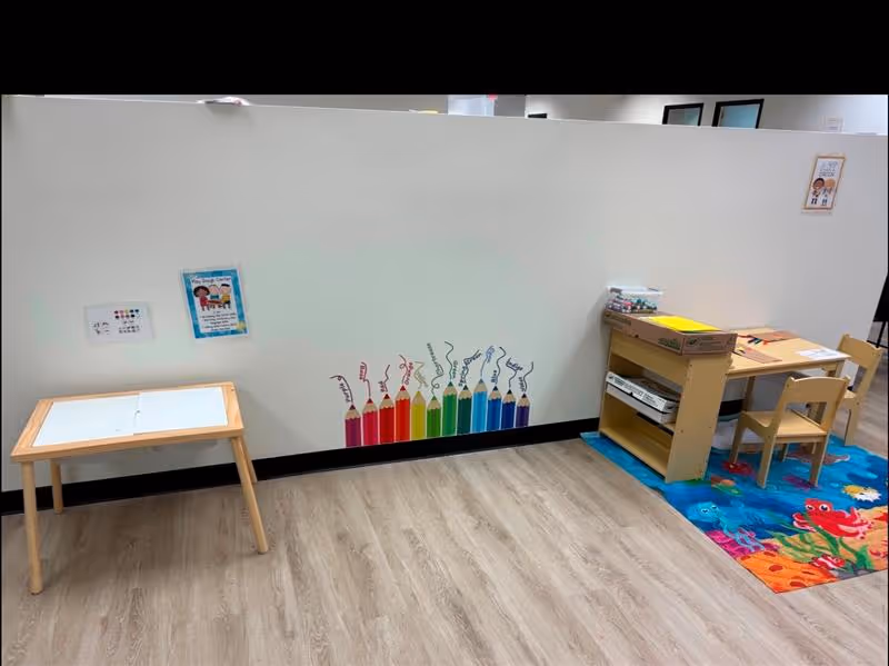 White partition wall in a bright therapy room with a small table and rainbow pencils.