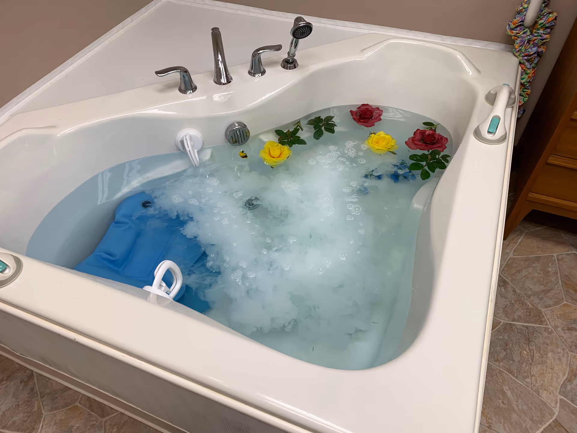 White whirlpool bathtub filled with bubbly water and floating colorful roses in a bathroom.