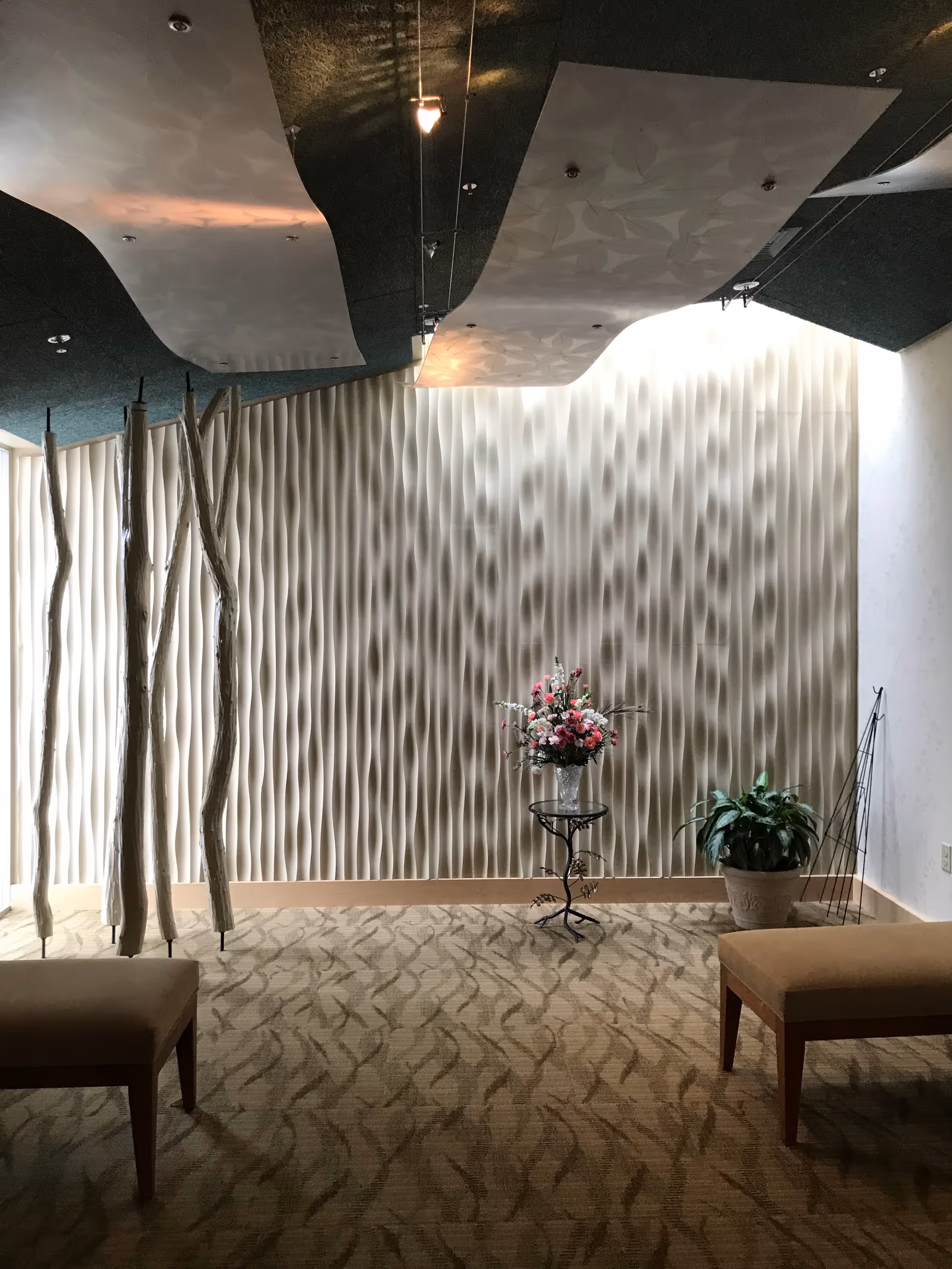Modern interior lounge with wavy wall panels, plants, and seating.